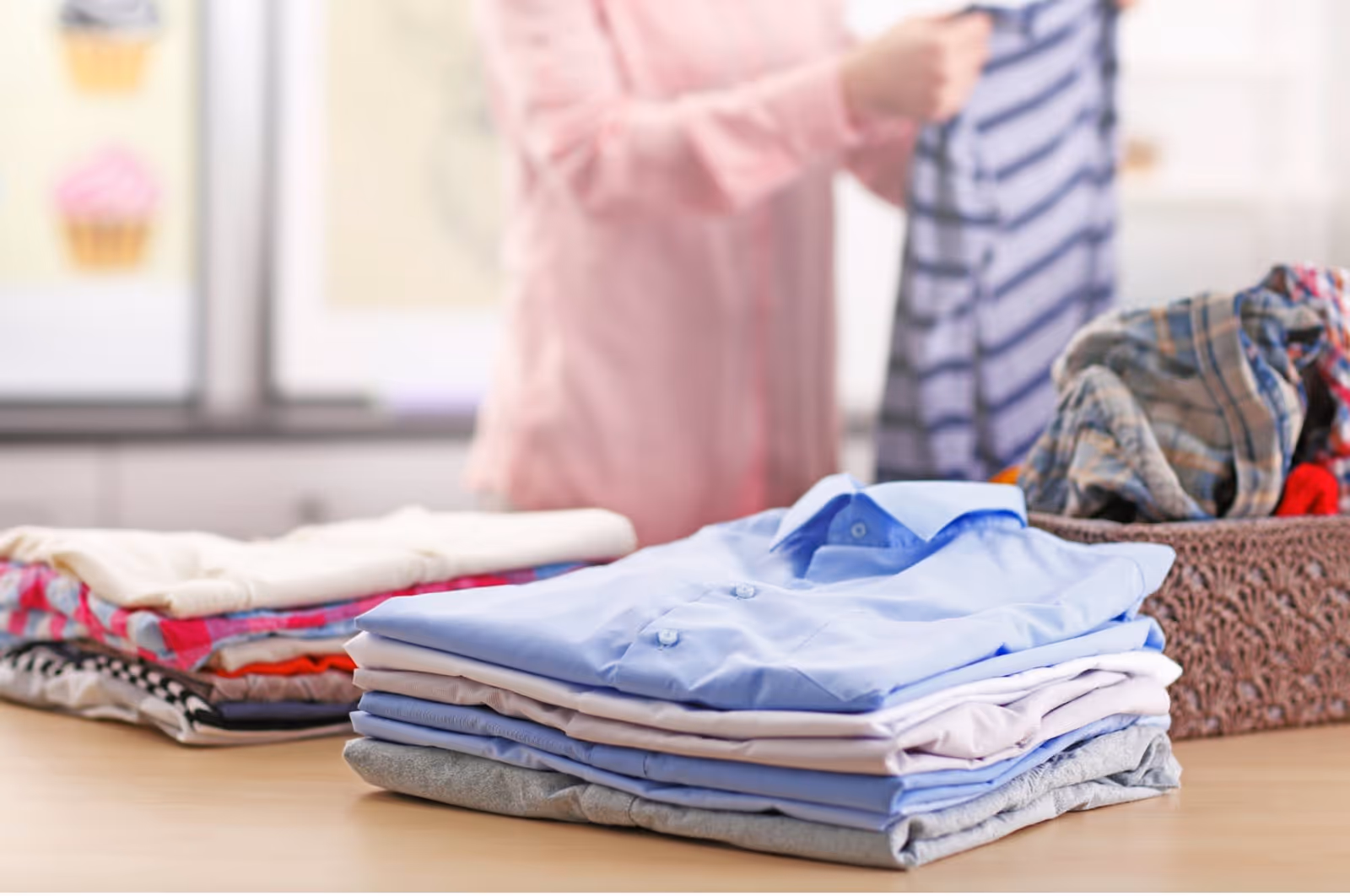 Stacks of folded clothes on a table with a blurred person in background.