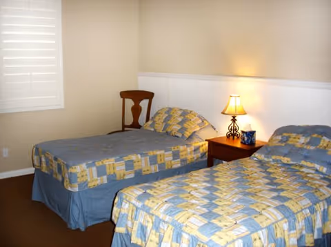 Two twin beds with patchwork quilts, a nightstand lamp, and a chair in a shared bedroom.