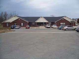 Red brick senior living facility with a parking lot and cars in front.