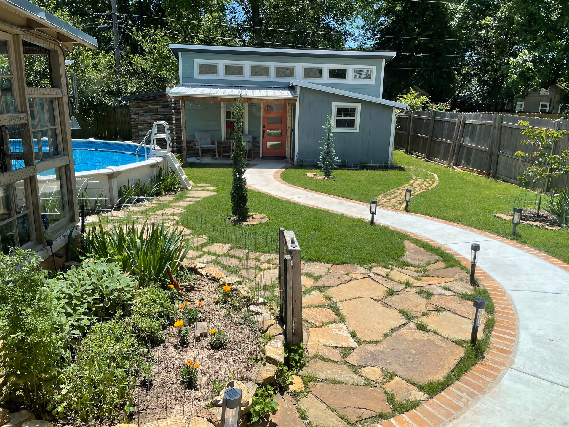A landscaped backyard with a pool, winding concrete path, and a modern blue shed.