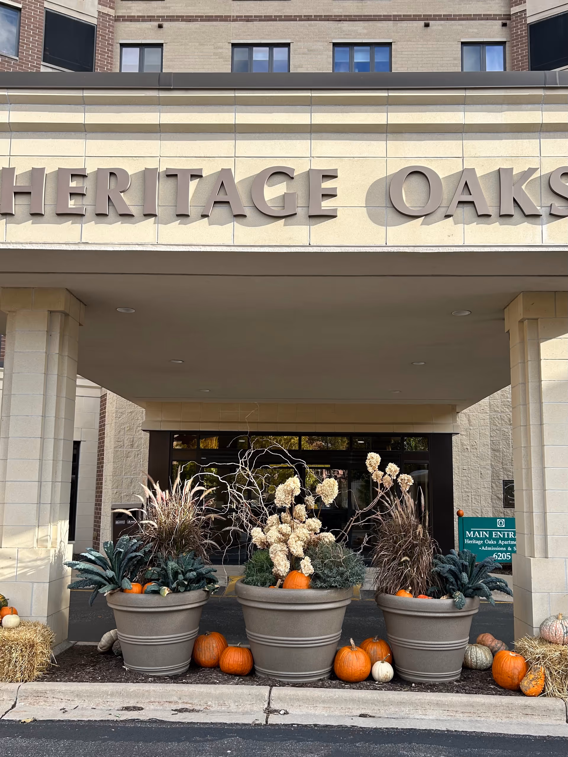Exterior entrance of Heritage Oaks with large planters and pumpkins beneath a covered entry.
