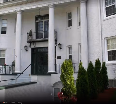 White-columned Candlelight Lodge entrance with stairs, a small balcony, and neatly trimmed shrubs.