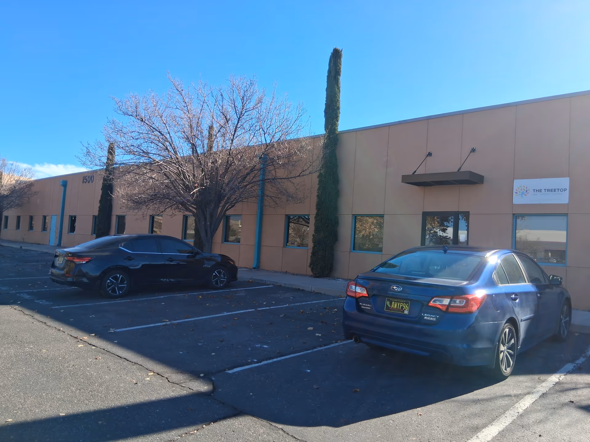 Exterior view of a tan building with parked cars and leafless trees.