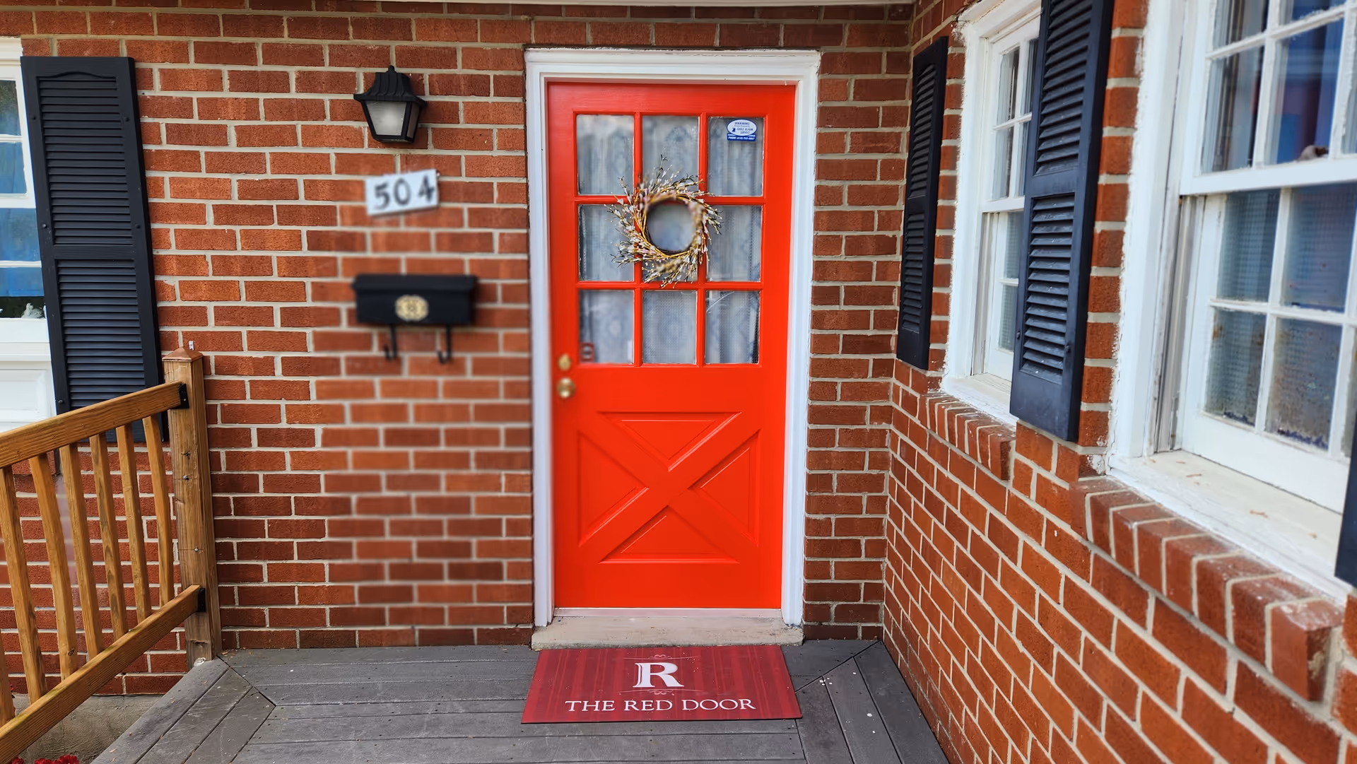 Bright red front door with a wreath on brick exterior.