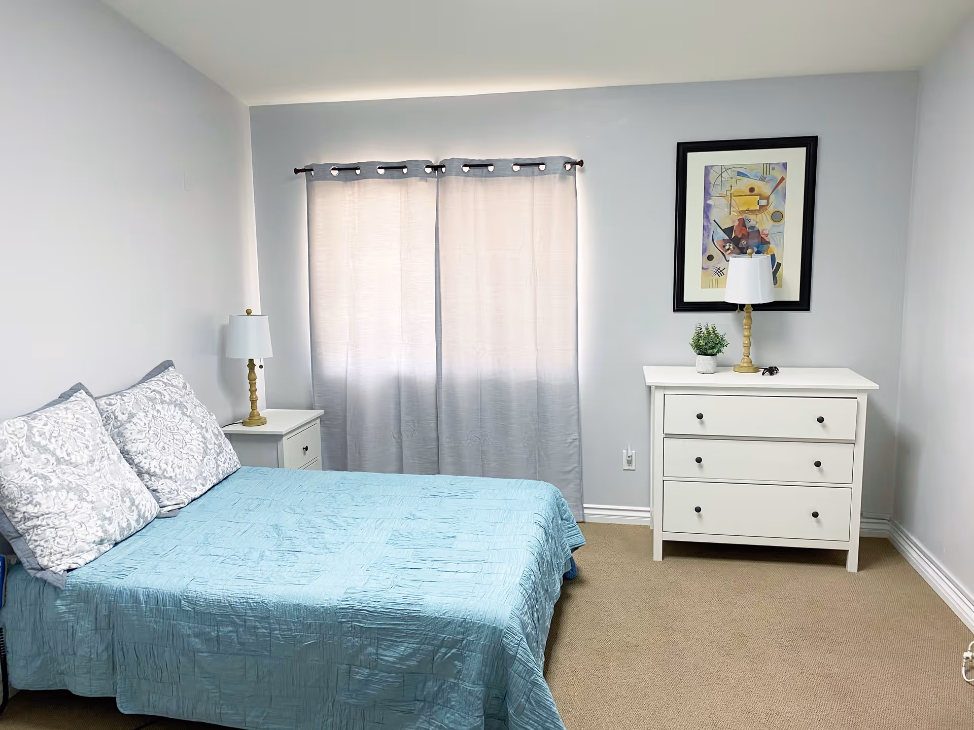 A cozy, neatly made bedroom with a bed, dresser, and soft curtains.