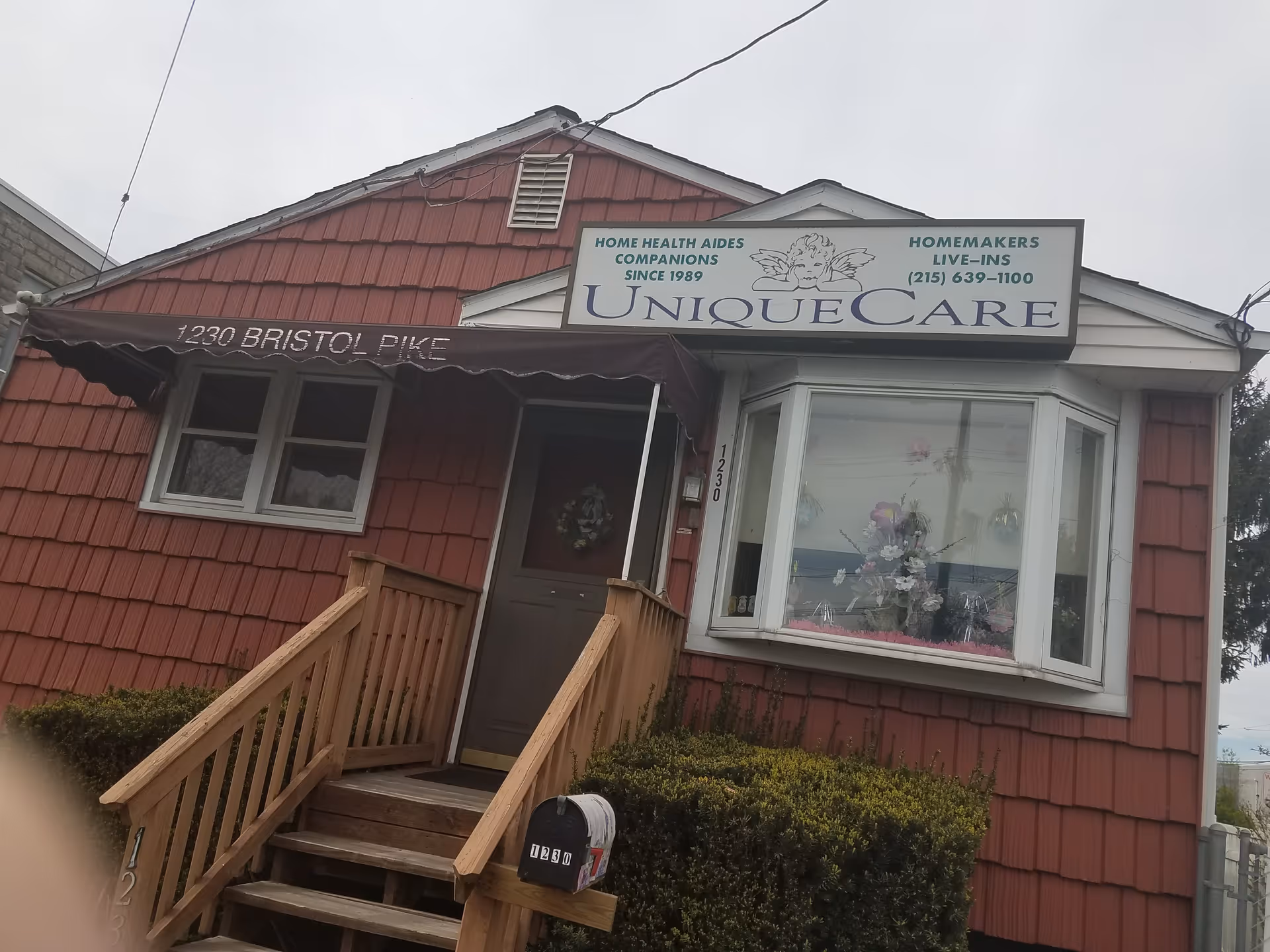Exterior of Unique Care senior facility with red siding, sign, and front stairs.