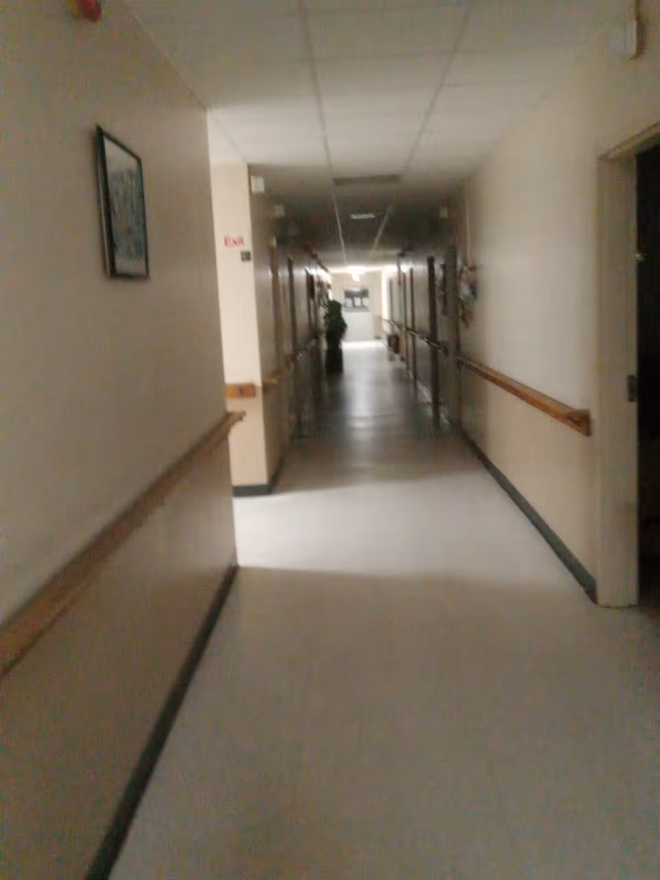 Dim hallway inside a senior care facility with handrails and doors along both walls.