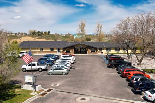 Front exterior of Monte Vista Hills Health Care Center with a parking lot filled with cars and an American flag in the foreground.