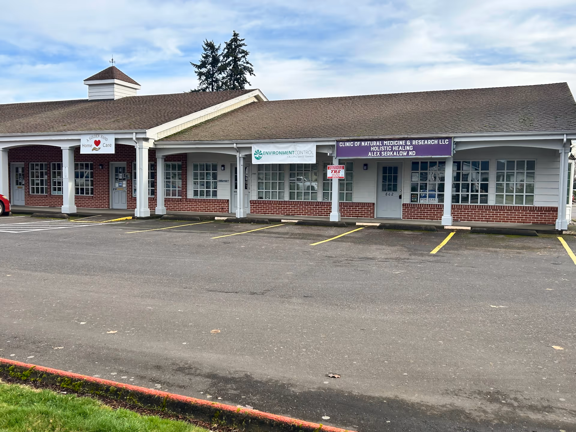 Front exterior view of a single-story storefront row with parking in front.
