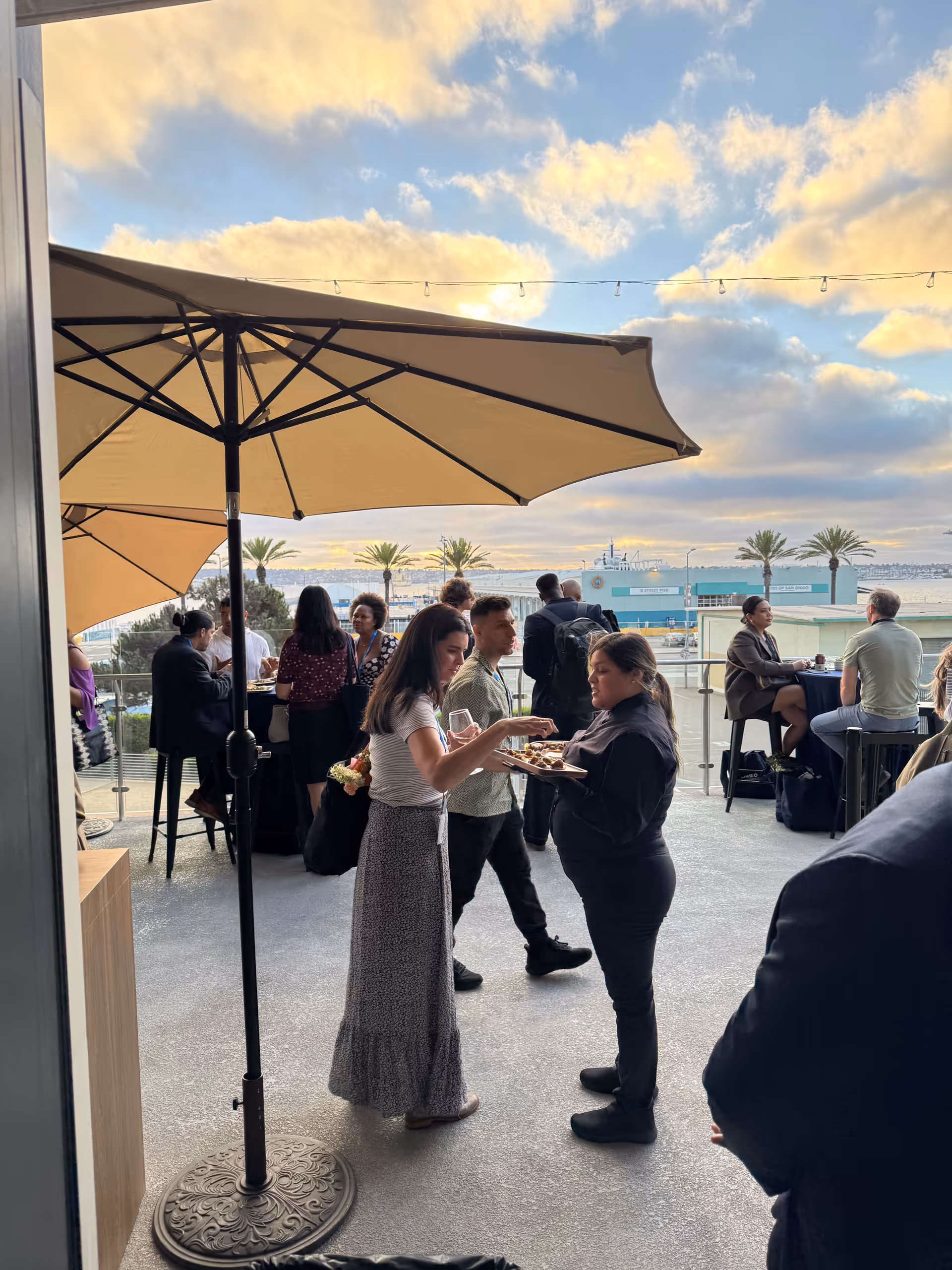 Residents and staff mingle on an outdoor patio by the water under large umbrellas.