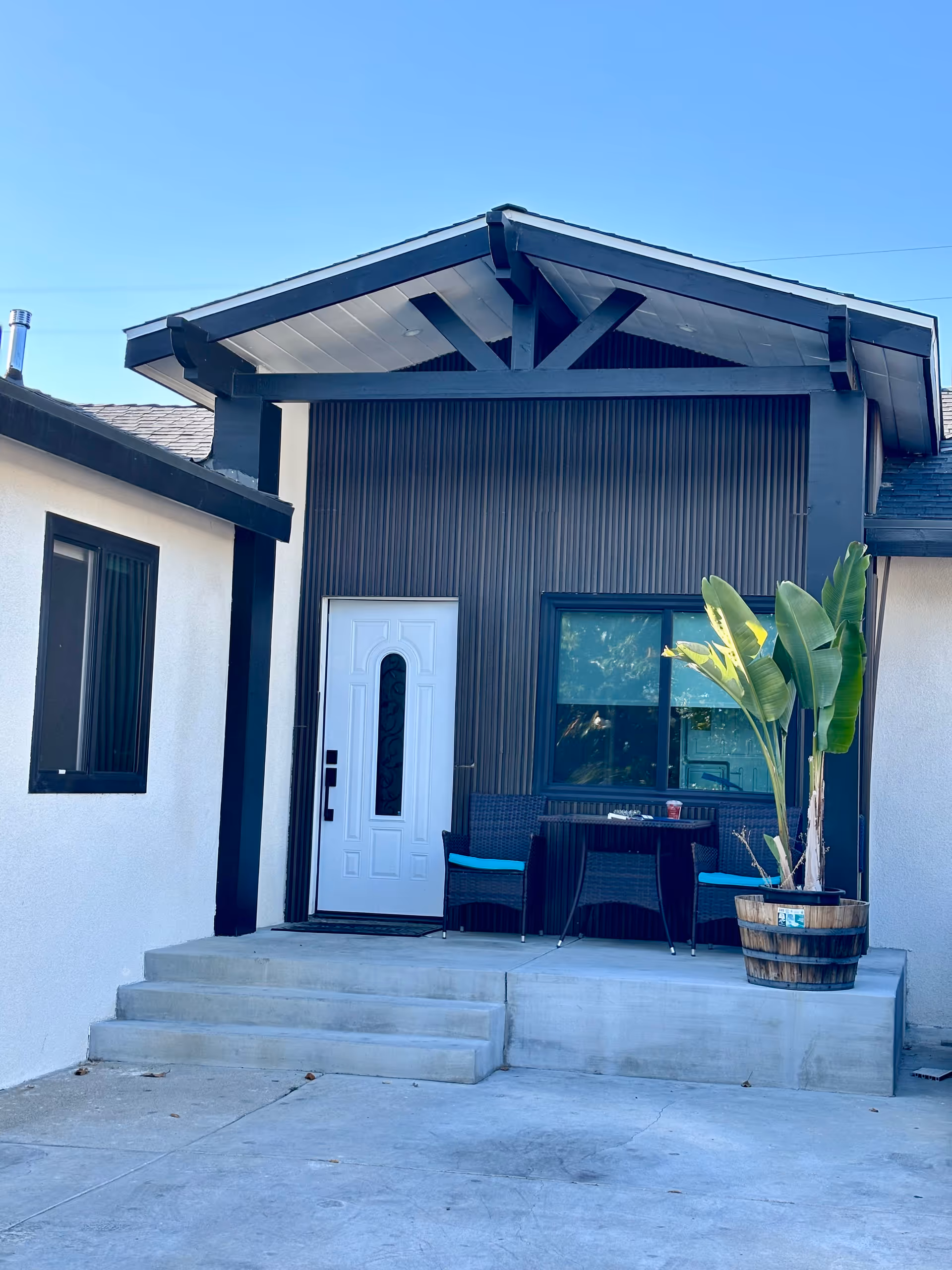 Modern front porch with a small table, two chairs, and a potted plant.