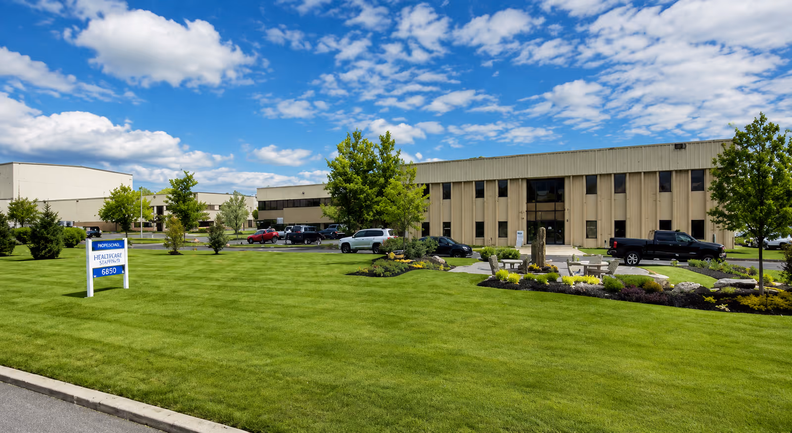 Exterior view of a beige healthcare building with manicured lawn, parking, and sign.