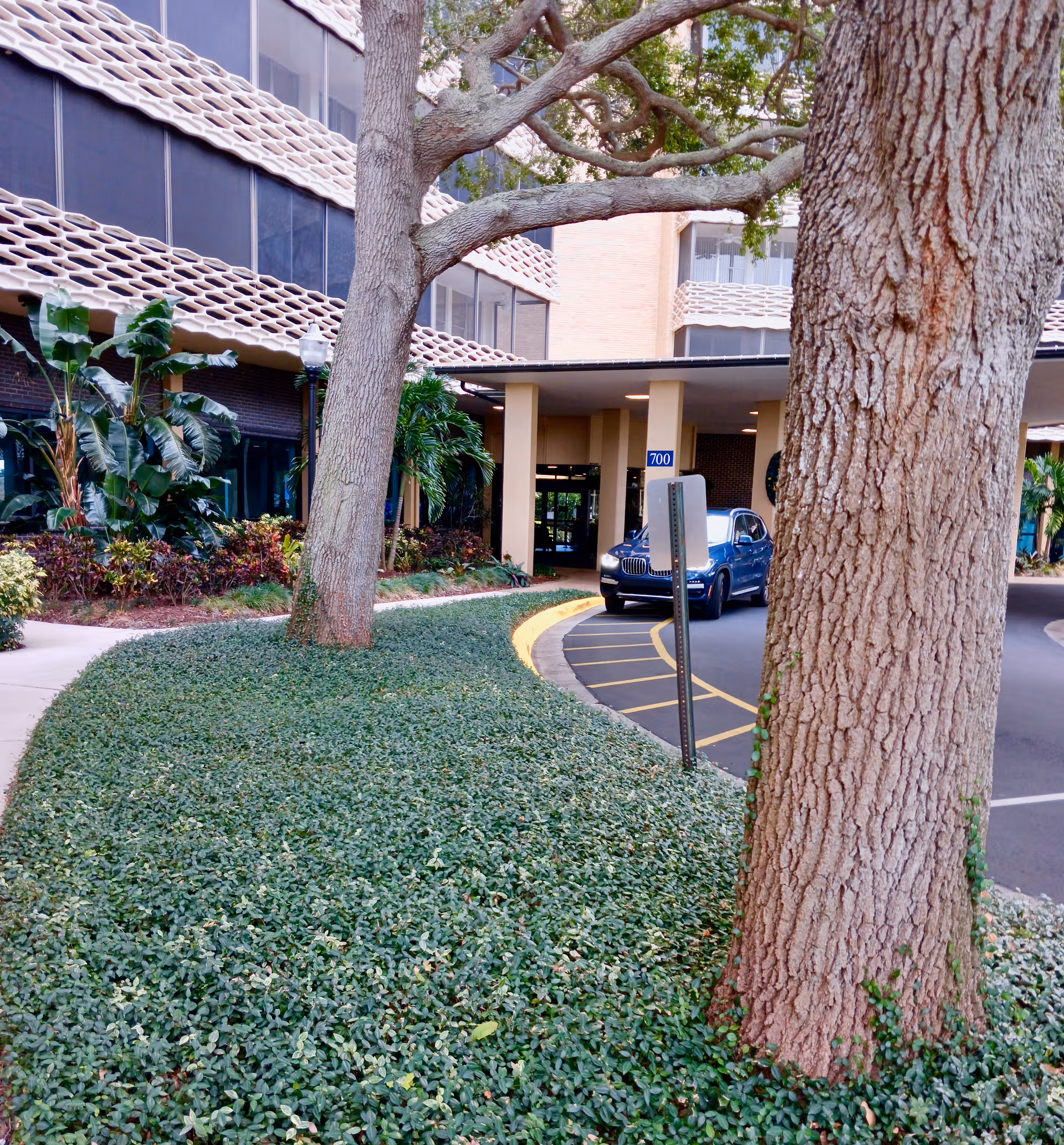 Exterior view of a memory care facility entrance with trees and landscaped grounds.