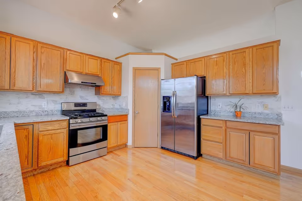 Bright kitchen with wooden cabinets, stainless steel refrigerator, stove, and granite countertops.