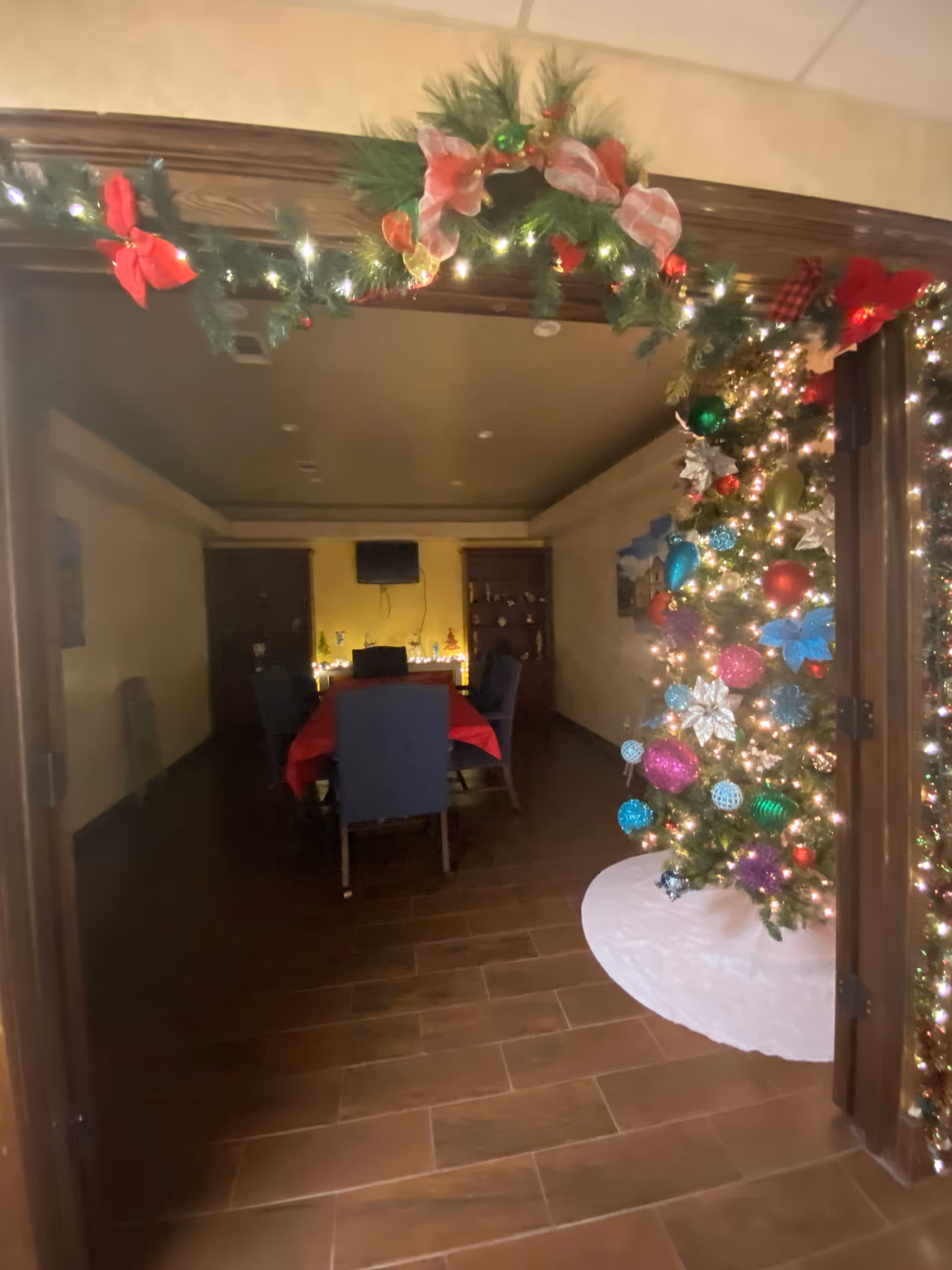 Indoor dining room decorated for Christmas with a garland arch and lit tree.