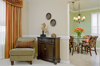 Cozy senior living room with a chair, cabinet, wall decor, and adjoining dining area.