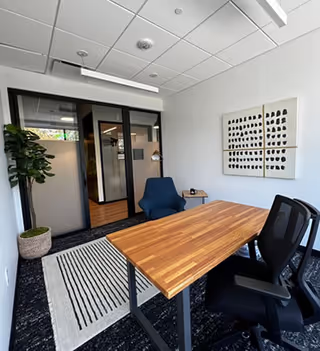 Modern, small office room with a wooden desk, chairs, plant, and wall art.