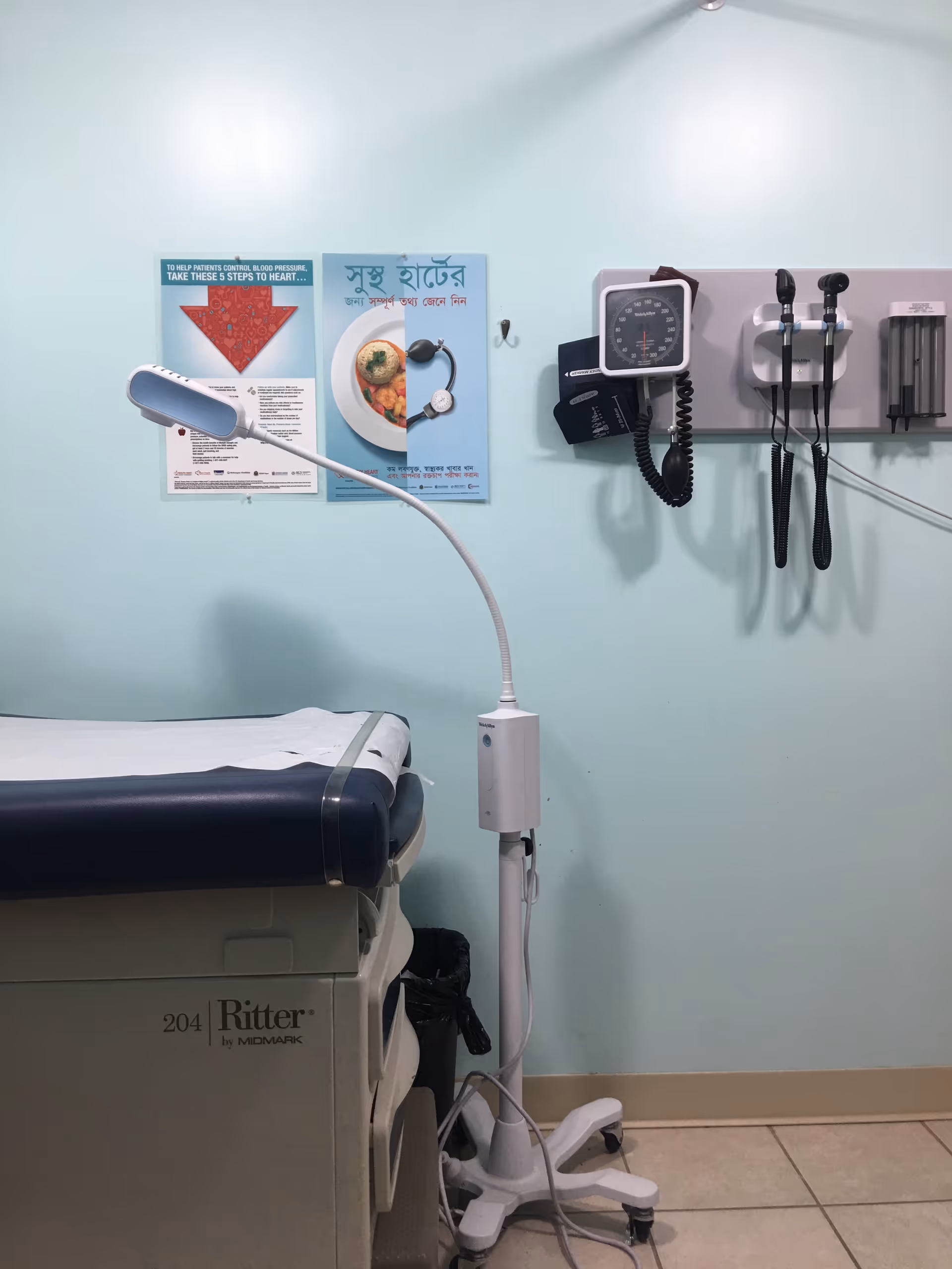 Examination bed and medical devices mounted on a pale blue wall in a clinical room.