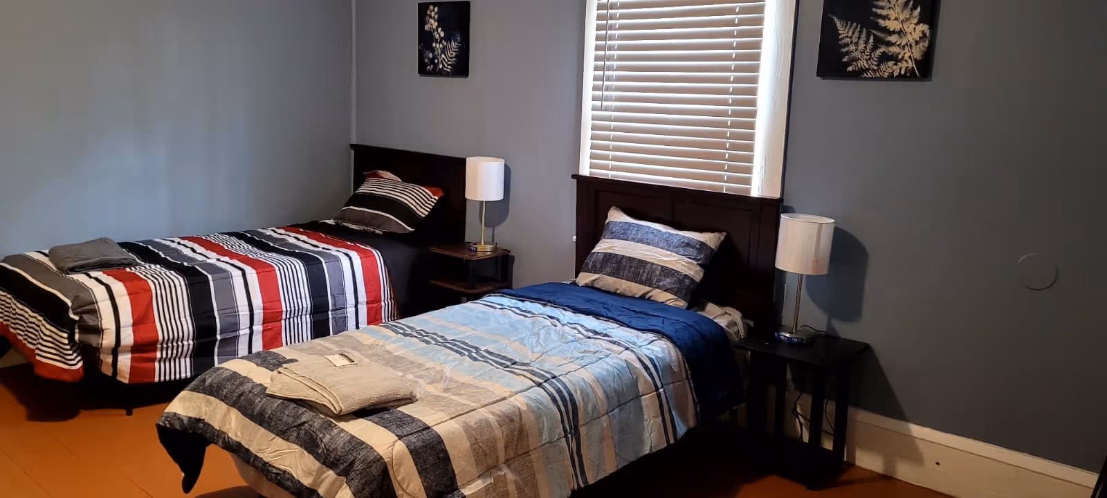 Two twin beds with striped quilts, matching nightstands, and a window with blinds in a bedroom.
