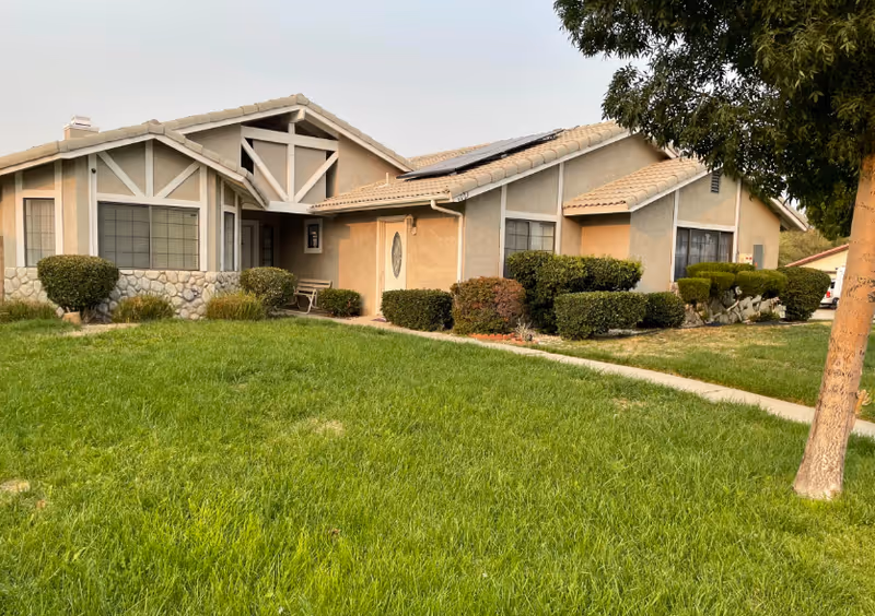 Single-story senior living facility exterior with manicured lawn and shrubs in front.