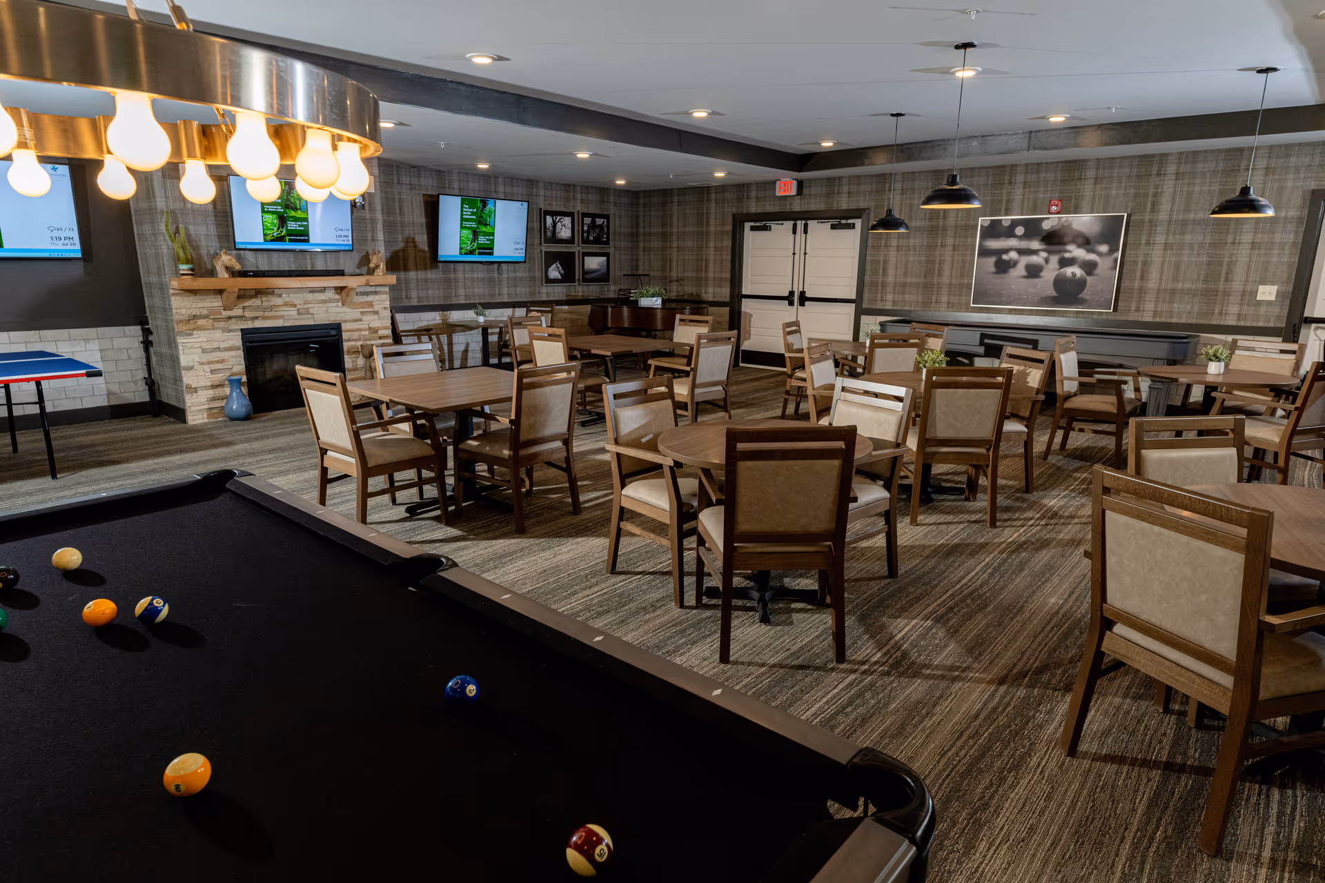 A spacious interior lounge with a pool table, multiple tables, and wall TVs.