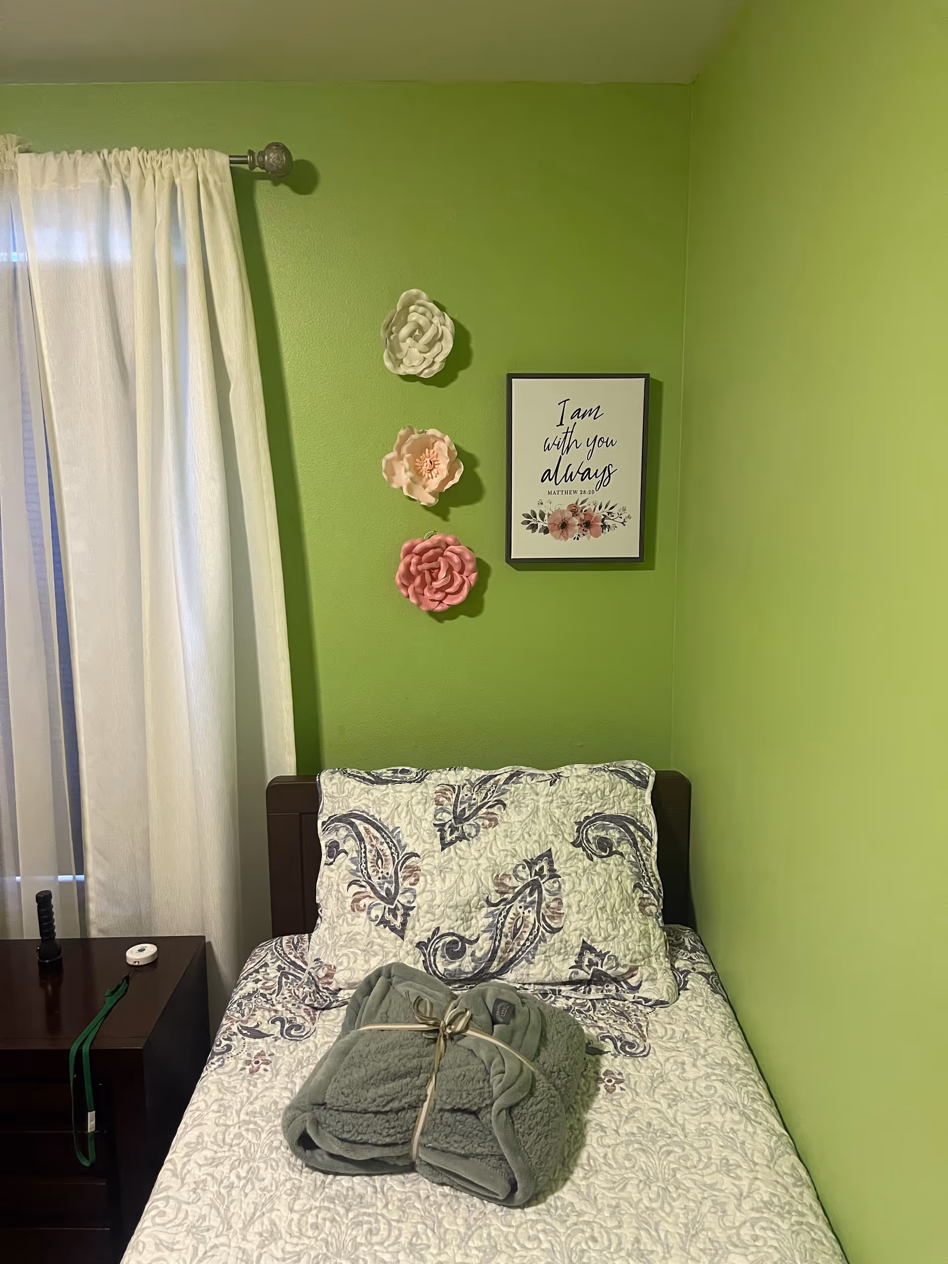 Bright green bedroom with a bed, quilt, wall decor, and a dark wooden nightstand.