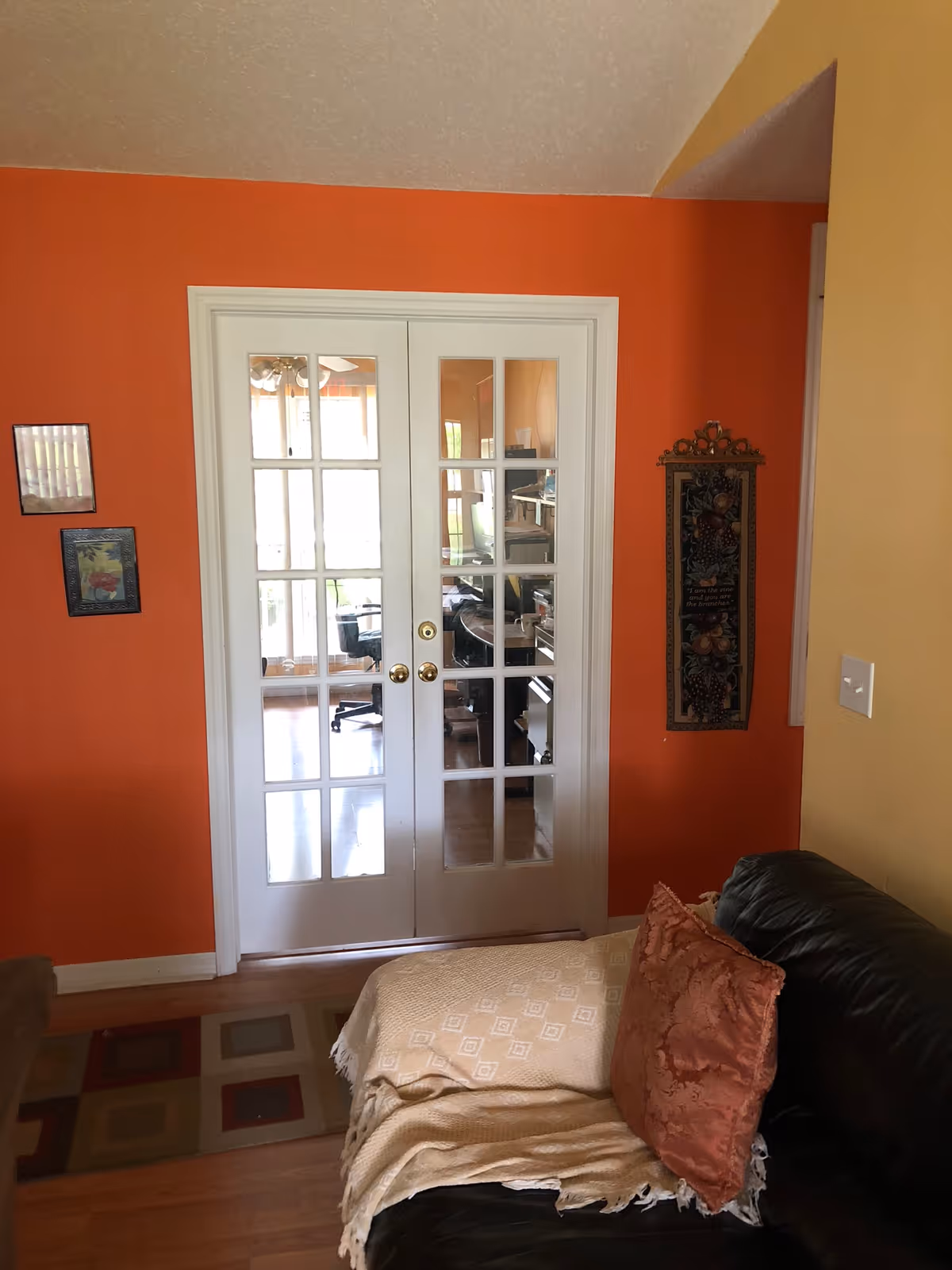 Living room with orange walls, glass French doors, and a black leather sofa with pillows.