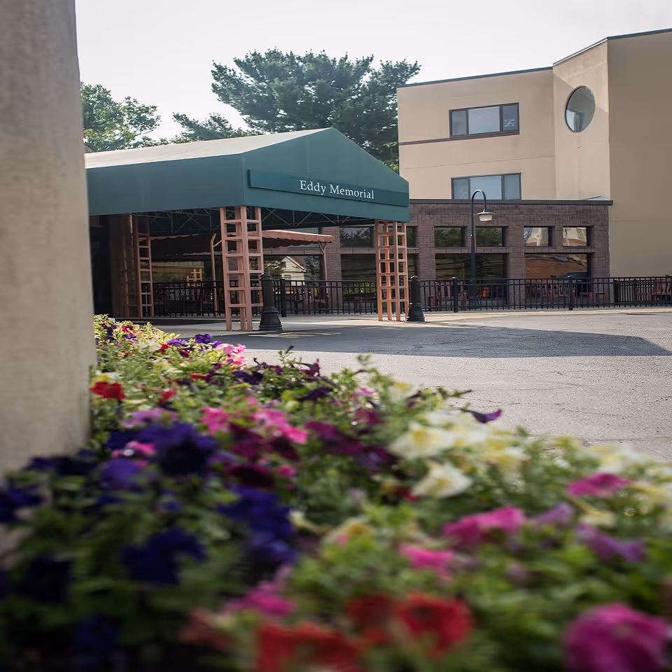 Front entrance of Terrace At Eddy Memorial with green canopy, building facade, and colorful flowers.