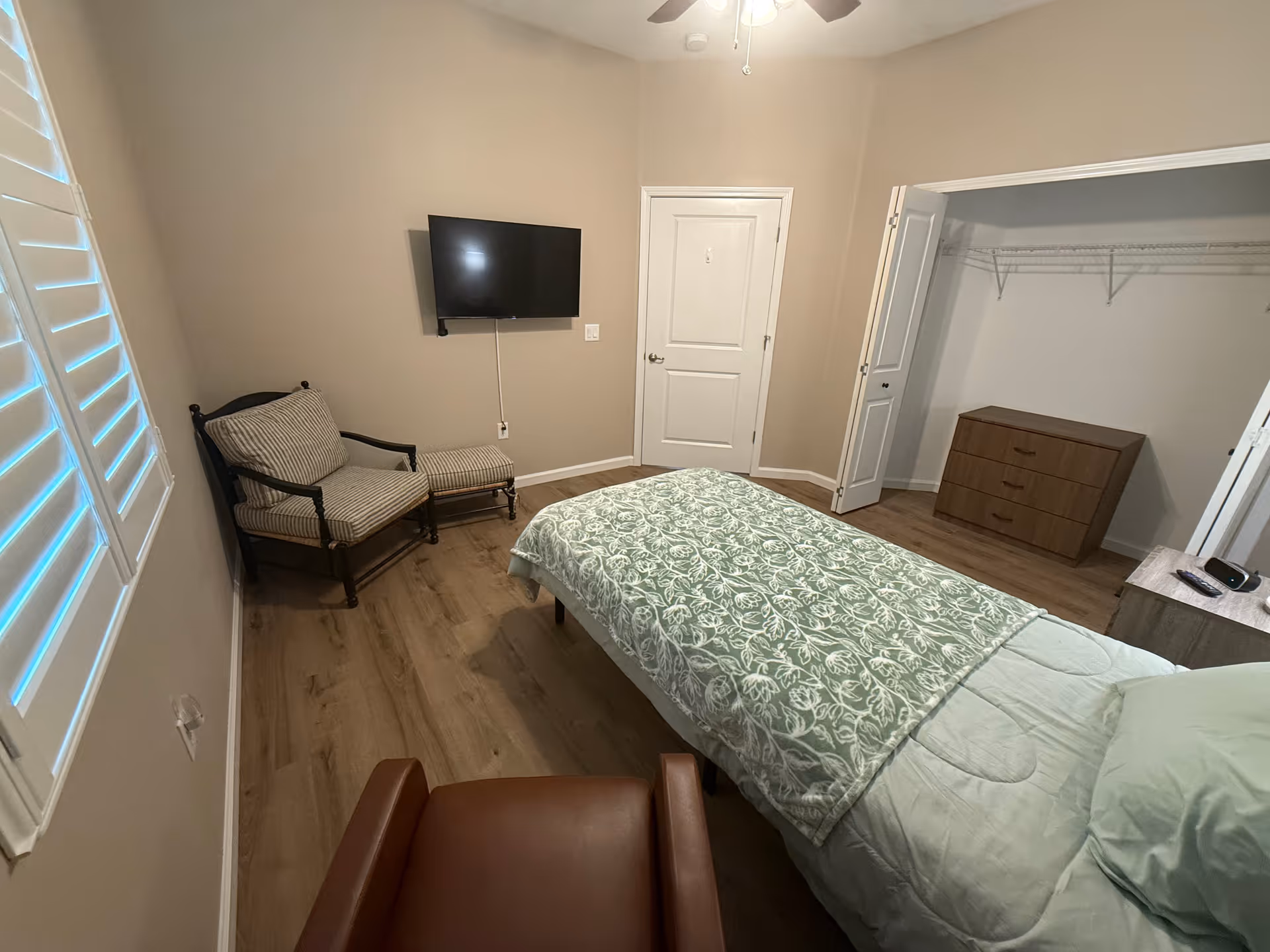 Neutral-colored bedroom with a bed, dresser, chair, TV, and open closet.