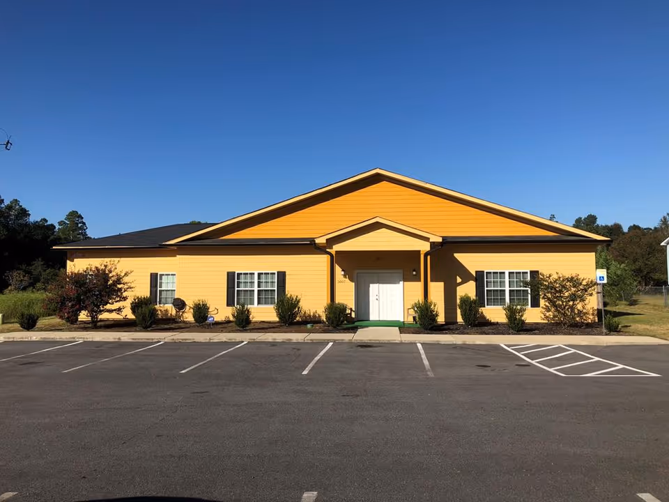 Single-story yellow building with a central entrance and empty parking spaces in front under a clear blue sky.