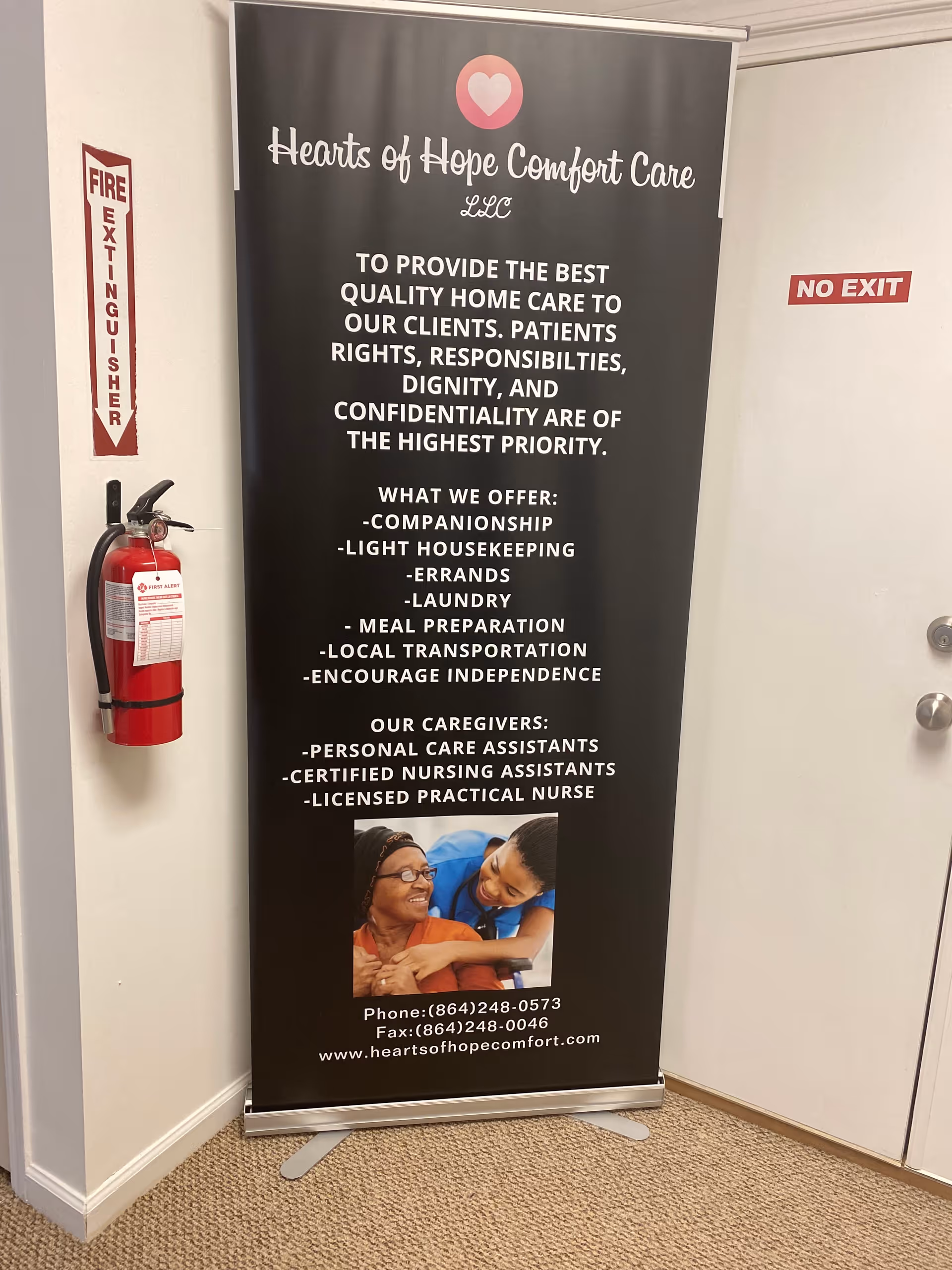 A tall vertical banner for Hearts of Hope Comfort Care stands in a hallway.