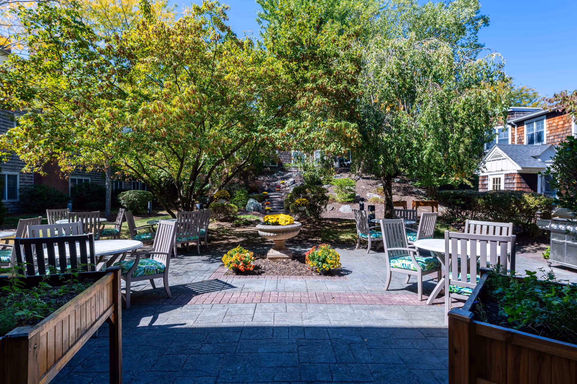 Outdoor courtyard with tables, chairs, and trees at Benchmark Senior Living at Hamden.