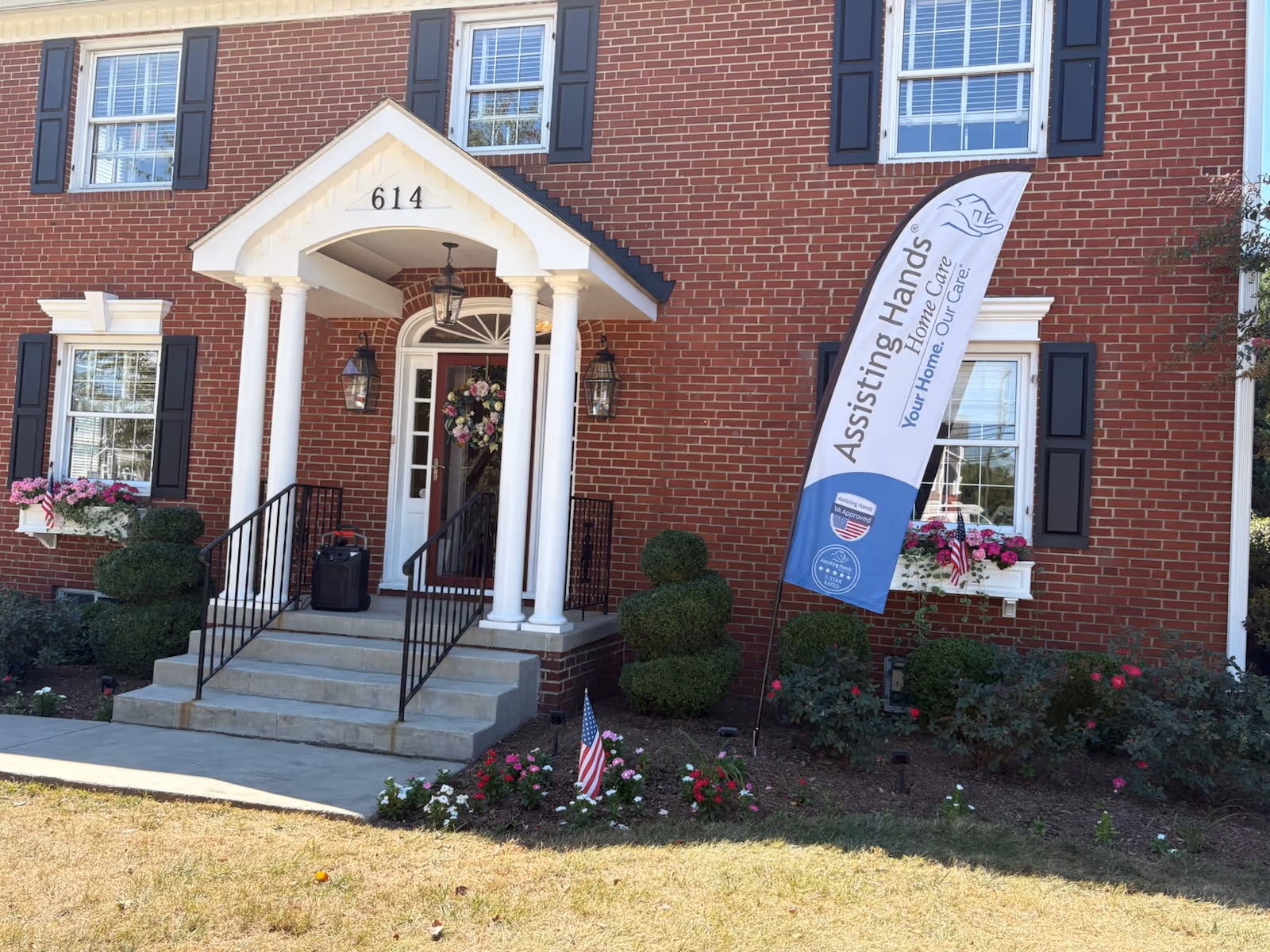 Brick building with a white-columned front porch and floral planters at the entrance.