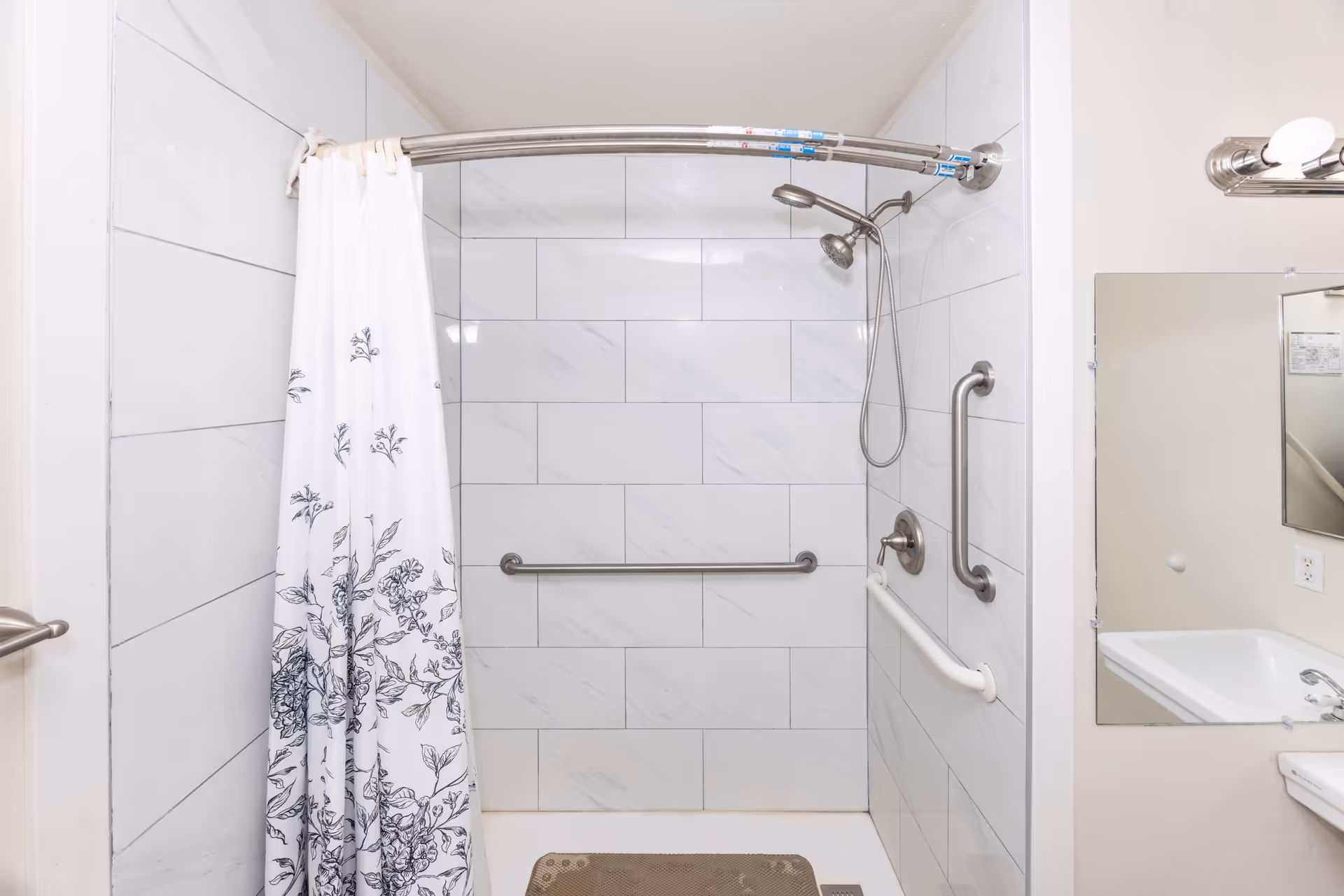 Accessible bathroom shower area with curved curtain rod, grab bars, and sink.