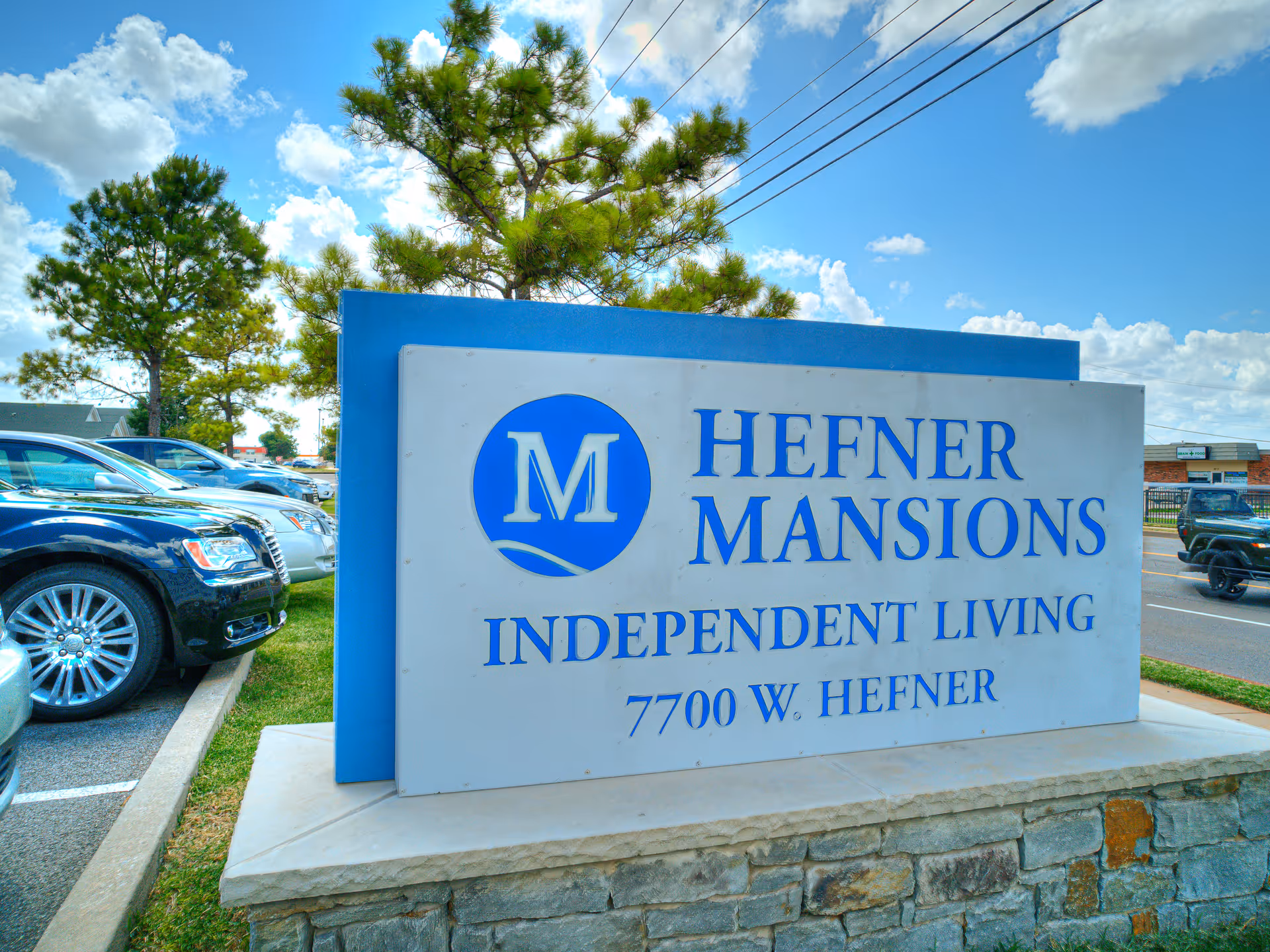 Exterior view of Hefner Mansions Independent Living sign with parked cars nearby.