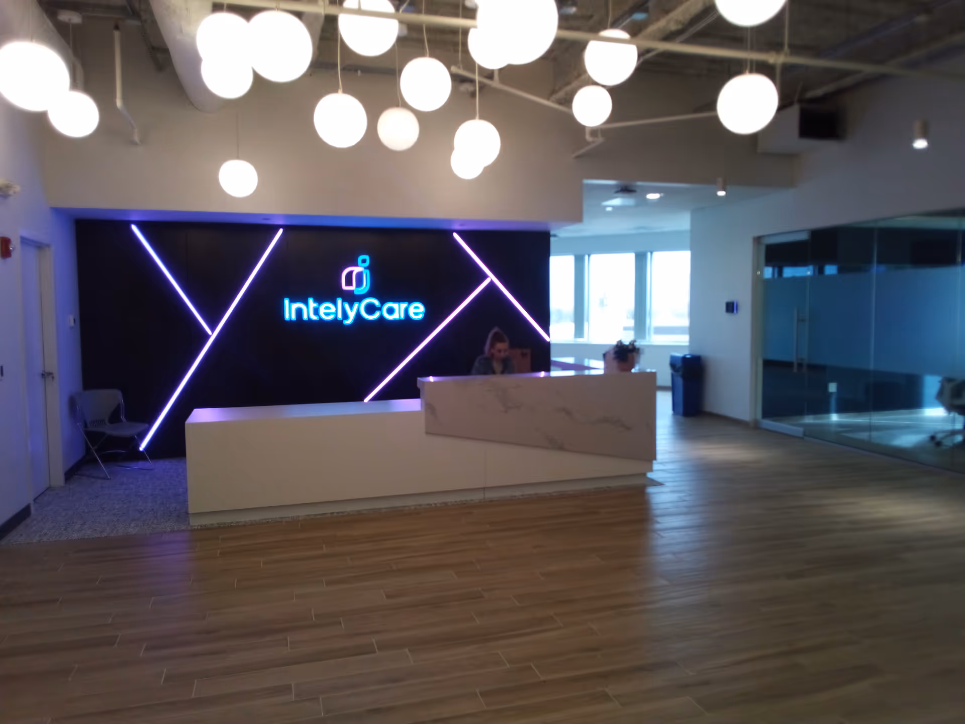 Modern reception area with a marble-front desk, glowing IntelyCare sign, and hanging pendant lights.