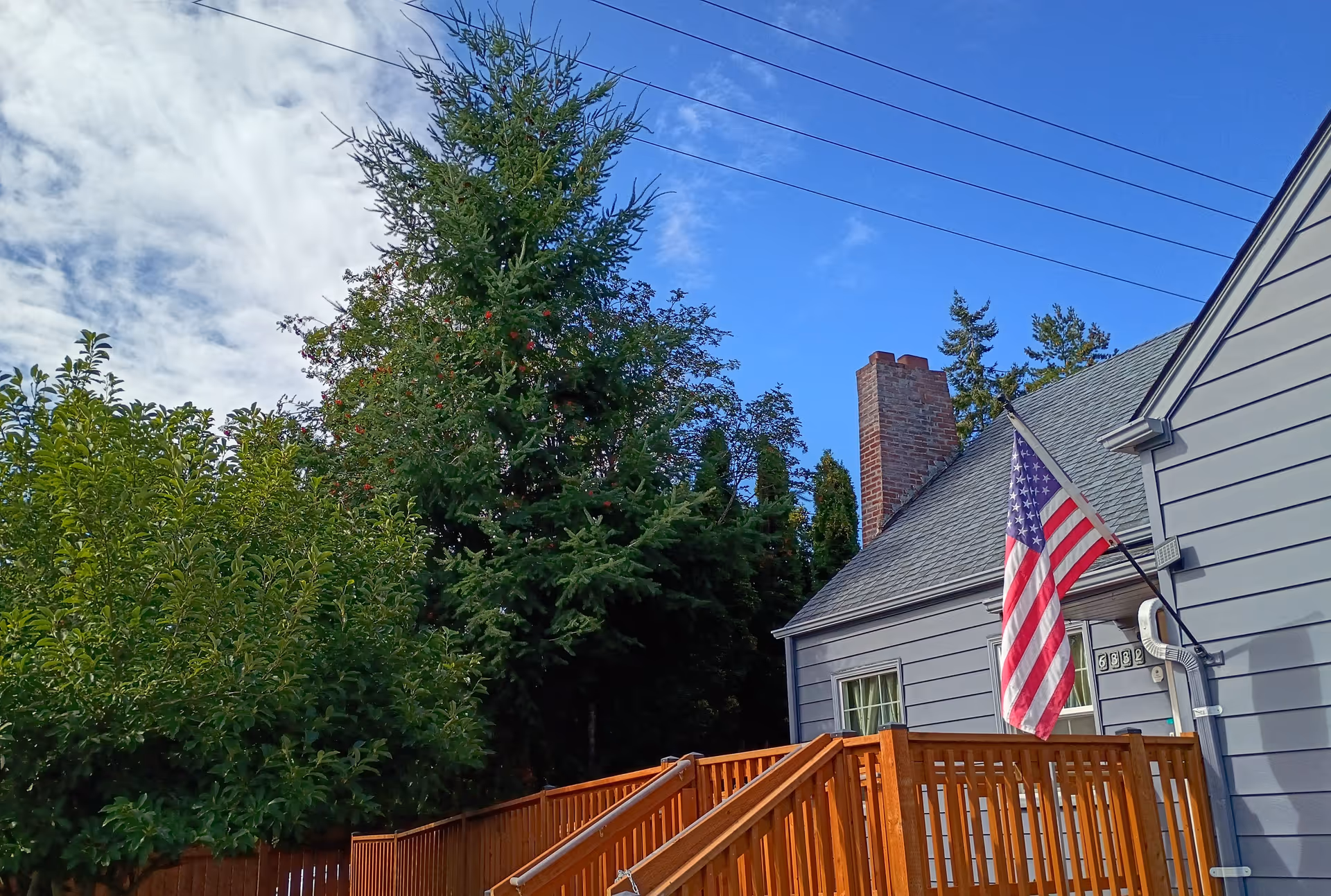 Exterior view of a gray building with wooden deck, flag, and surrounding trees.