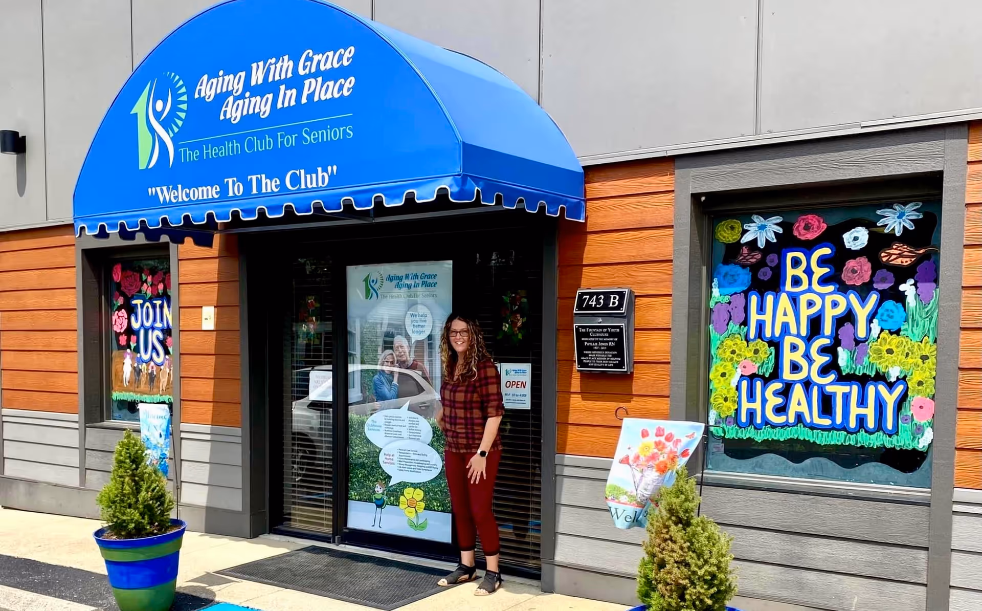 Entrance to Aging With Grace facility with blue awning and a woman outside.