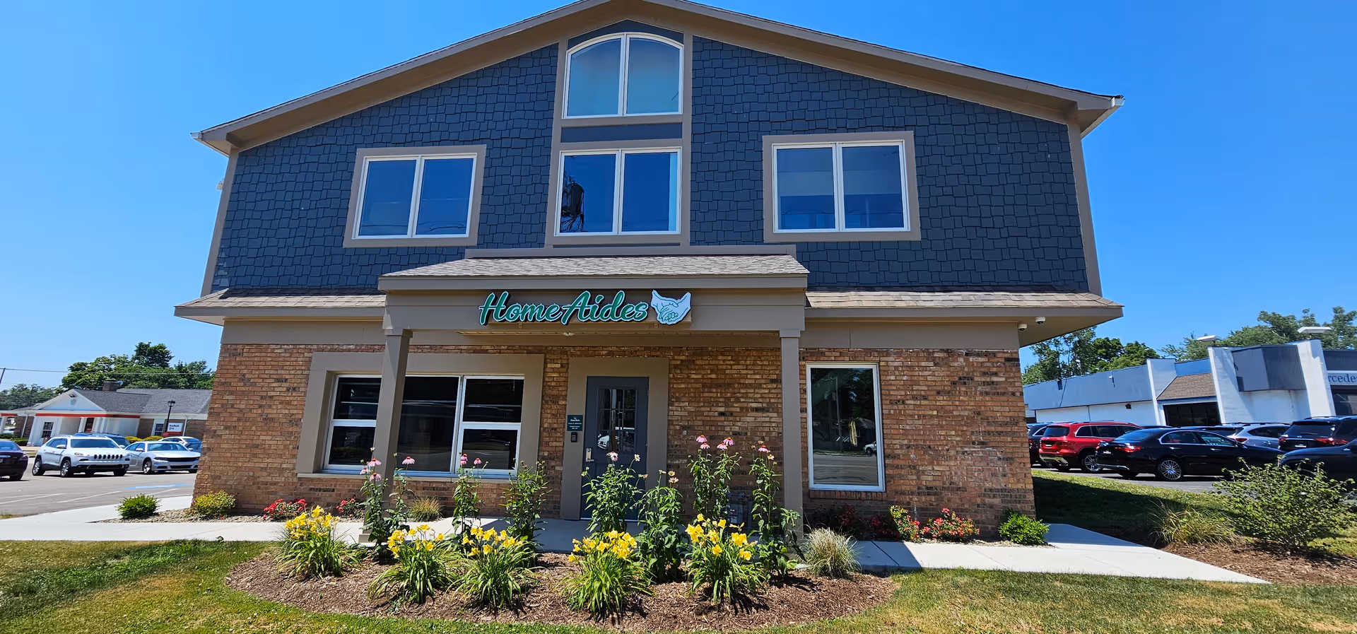 Two-story building with HomeAides sign, brick base, blue siding, and landscaped front.