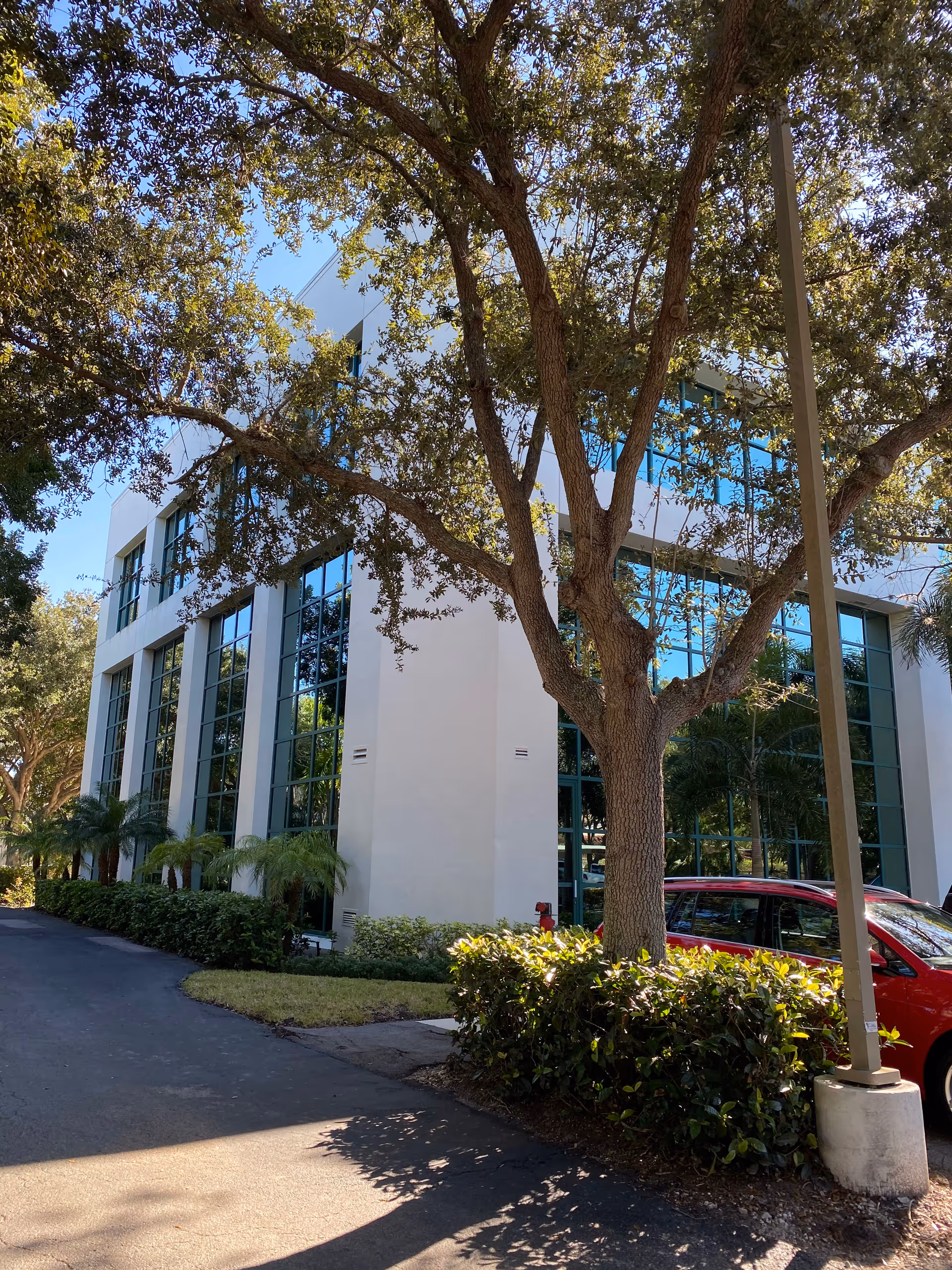 Modern senior living building exterior with tall glass windows, trees, and a parked red car.