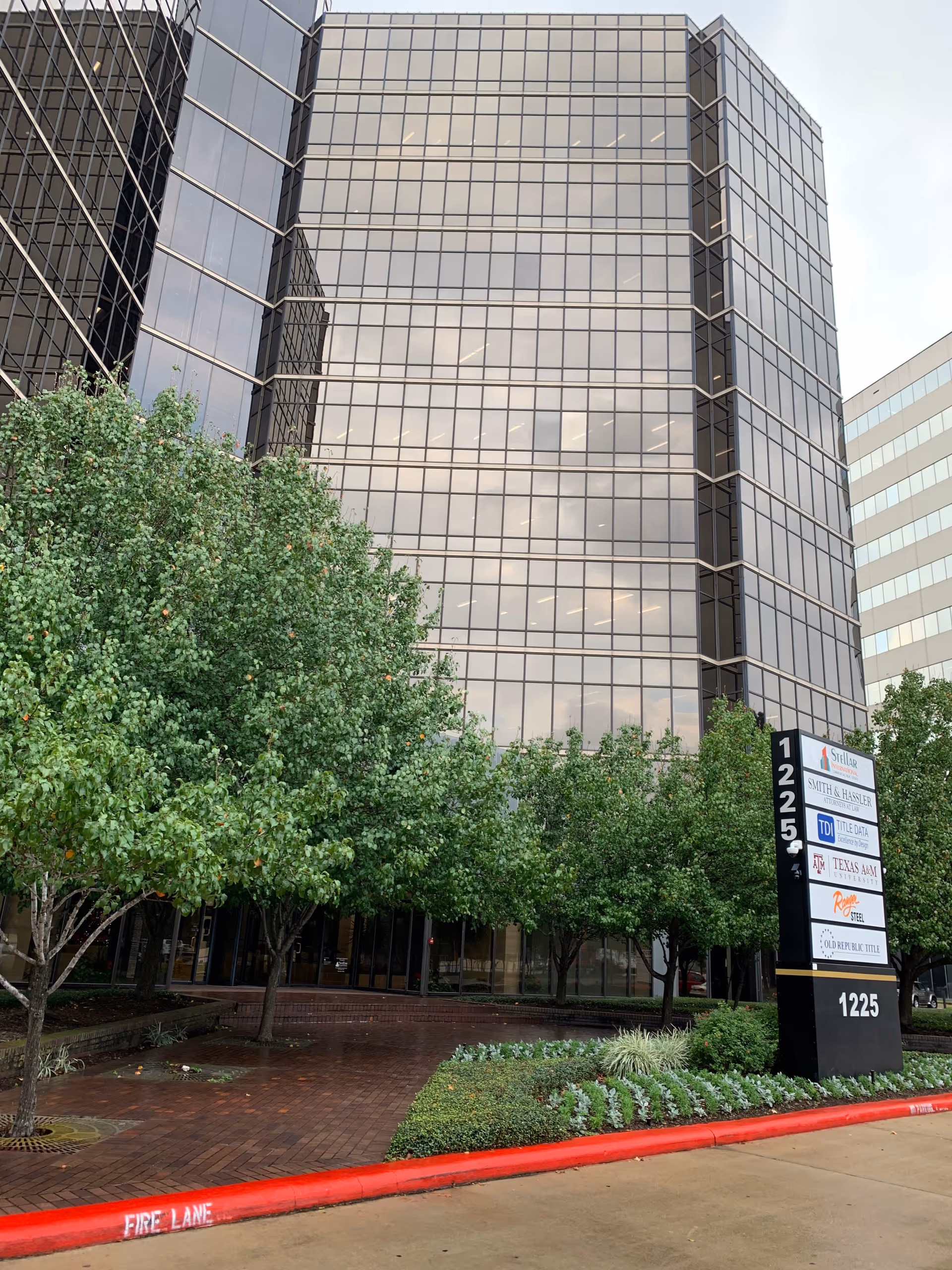 Tall glass-front office building with trees and a sign
