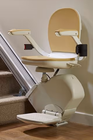 Beige stair lift chair attached to an indoor carpeted staircase in a senior living facility.