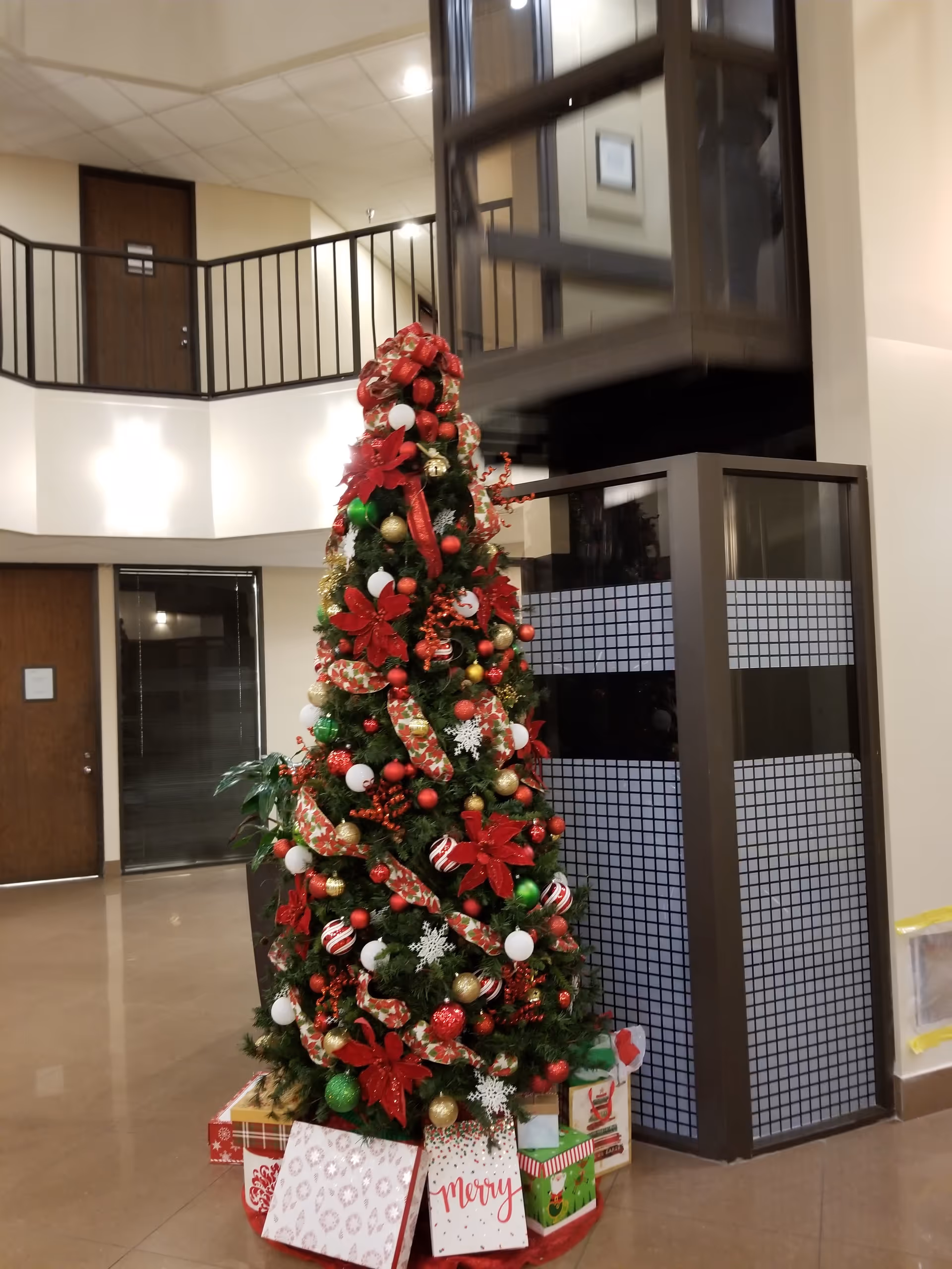 Decorated Christmas tree with red ribbons and gifts stands in Citizen Care Home Health lobby.