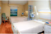 Two hospital-style beds in a senior care patient room with monitors and curtains.