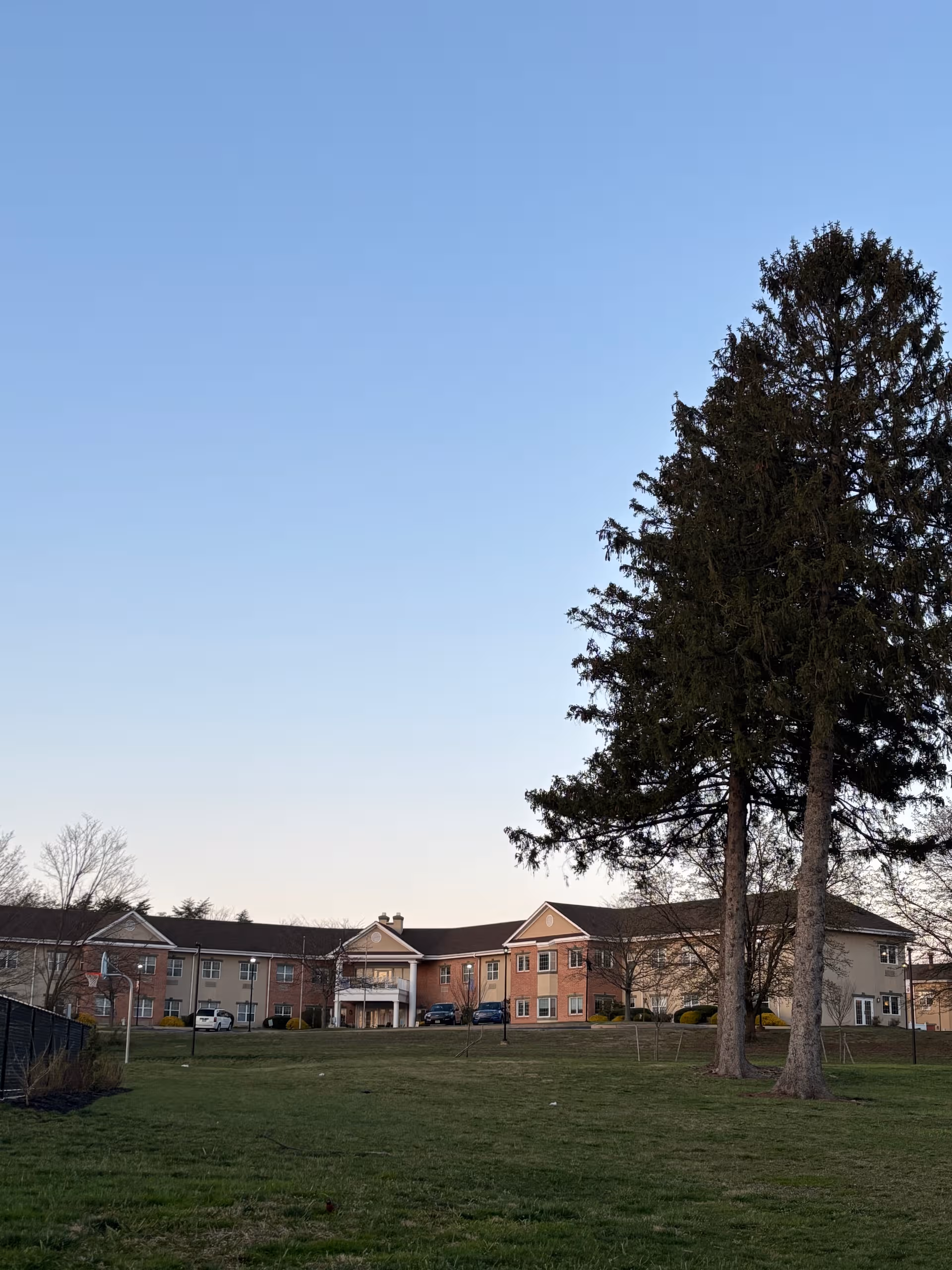 Exterior view of a senior living facility with a lawn and tall trees.