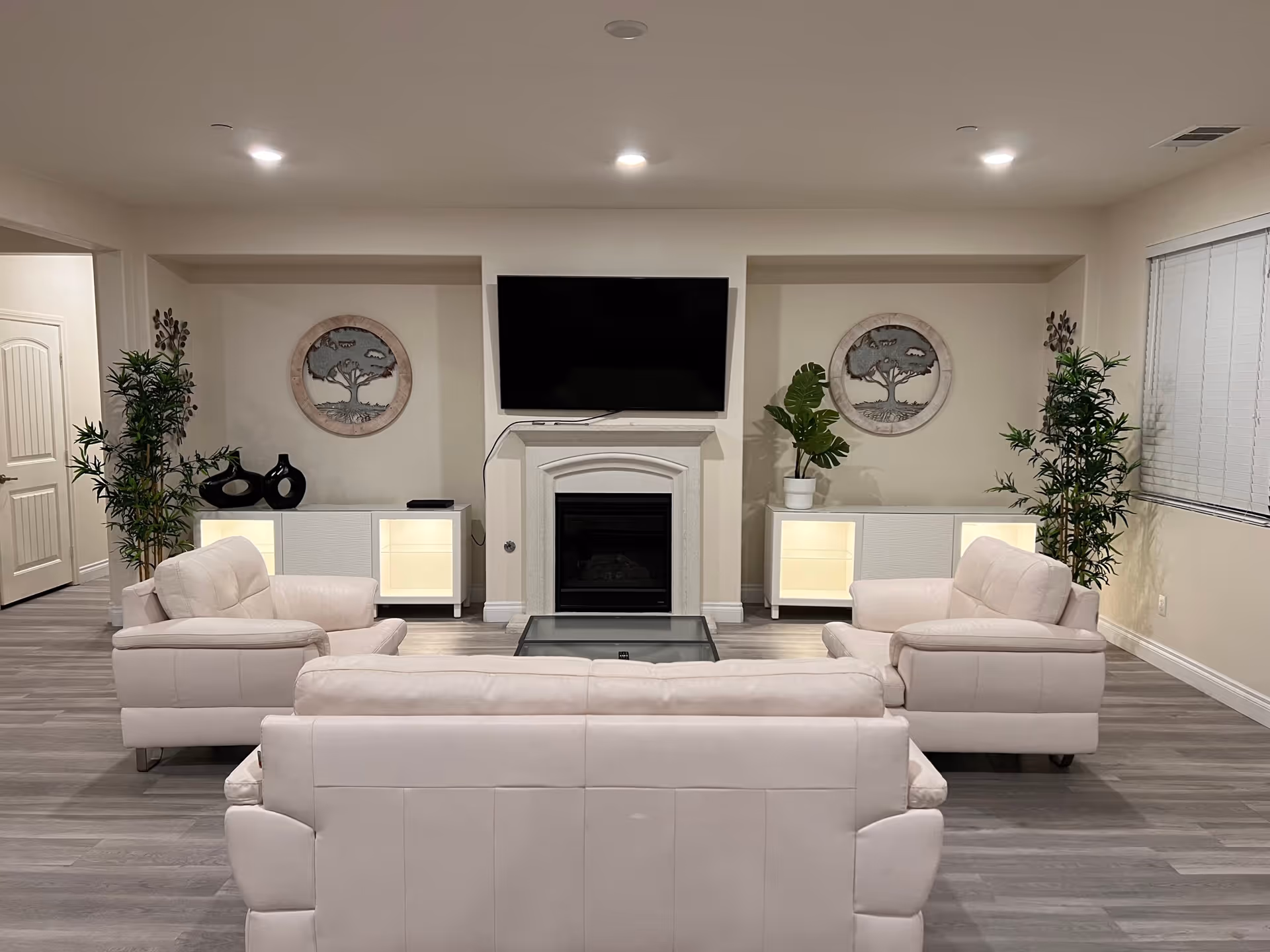Modern living room with beige sectional sofas, a coffee table, fireplace, mounted TV, and plants.