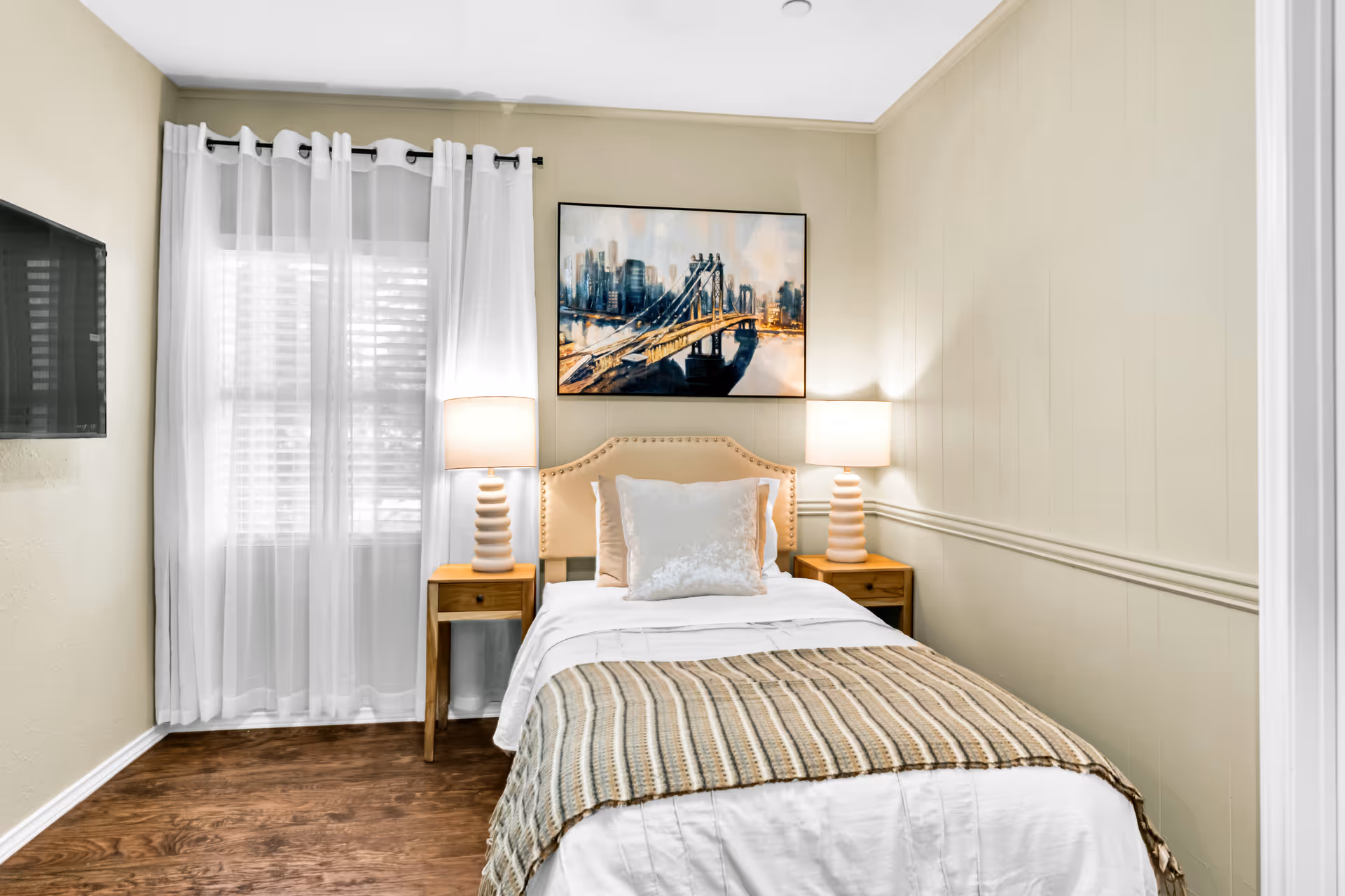 Cozy senior living bedroom featuring a bed, twin nightstands, lamps, and a window with curtains.