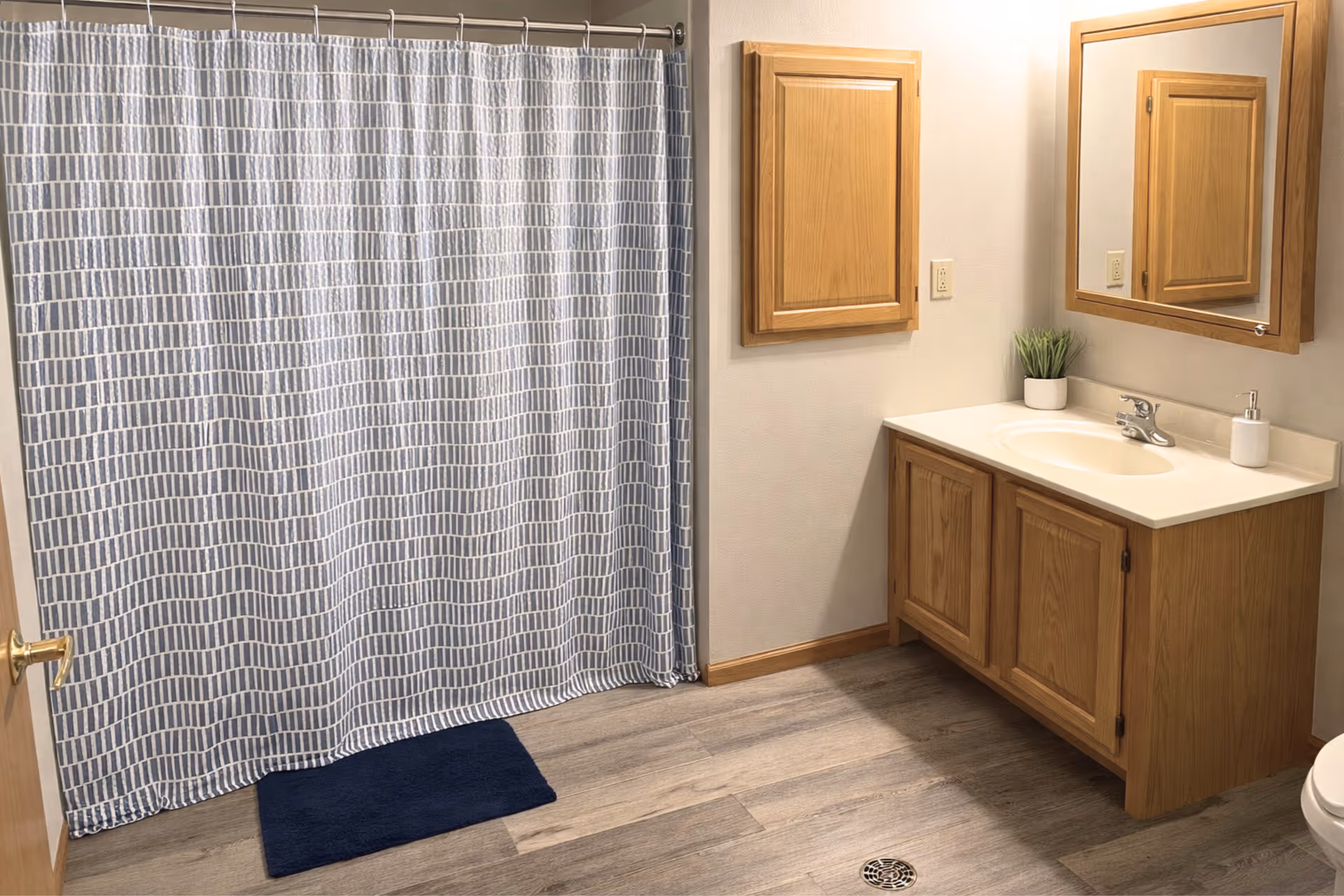 Senior living bathroom with wooden vanity, mirror, shower curtain, and blue mat.
