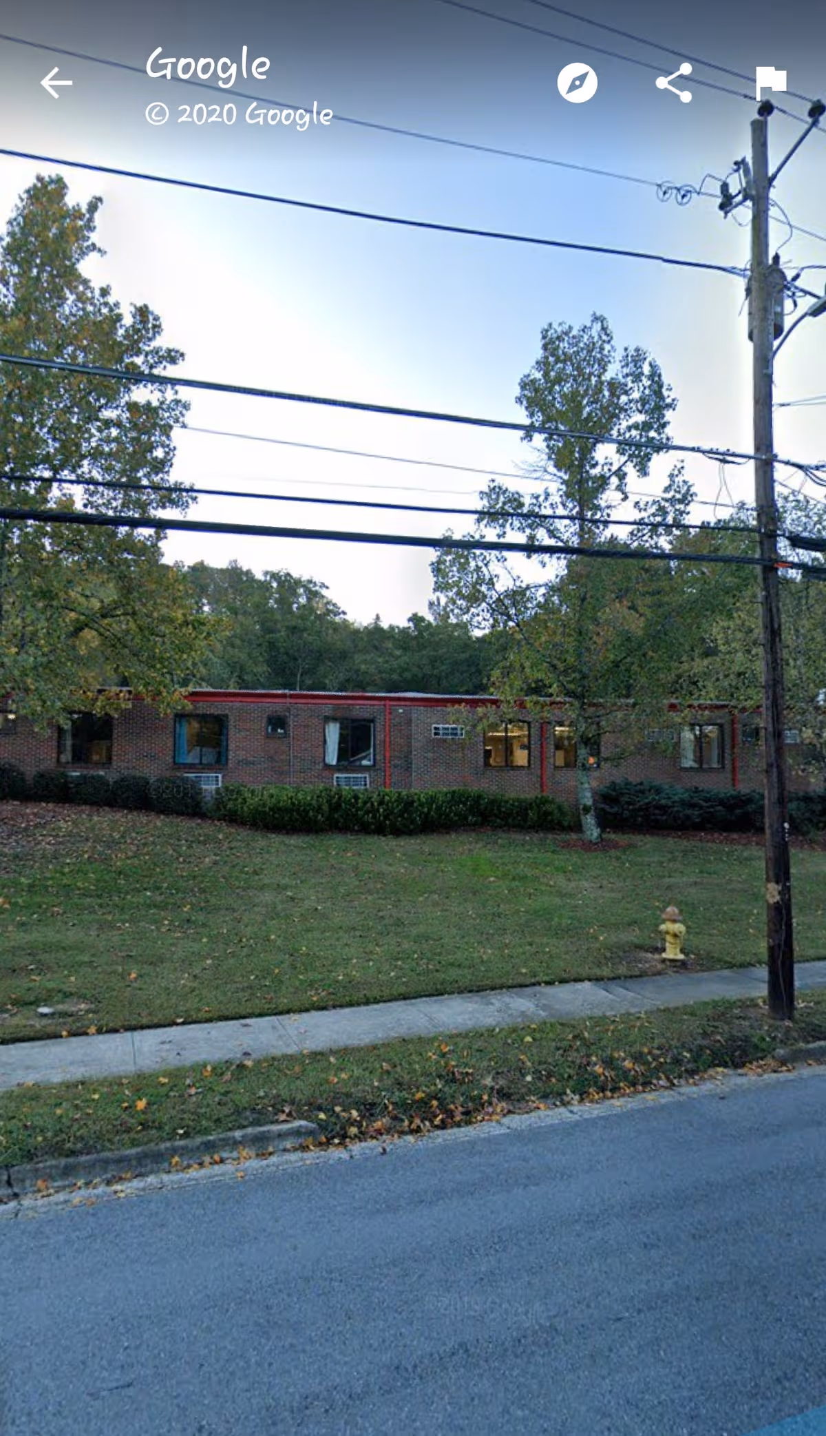 Exterior view of a brick senior living facility with trees, power lines, and a sidewalk.
