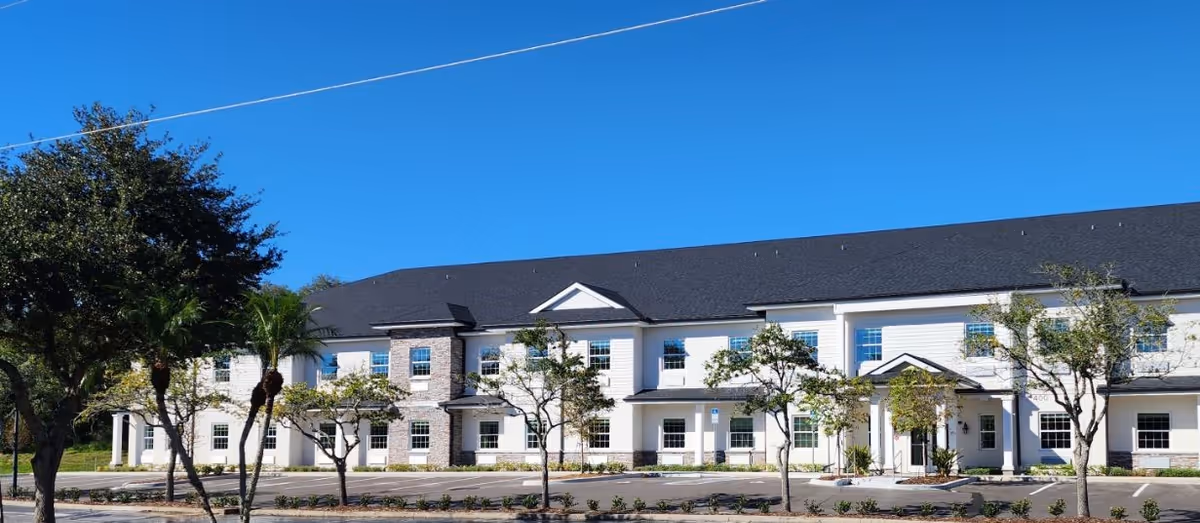 Exterior view of a two-story senior living facility with trees and a blue sky.